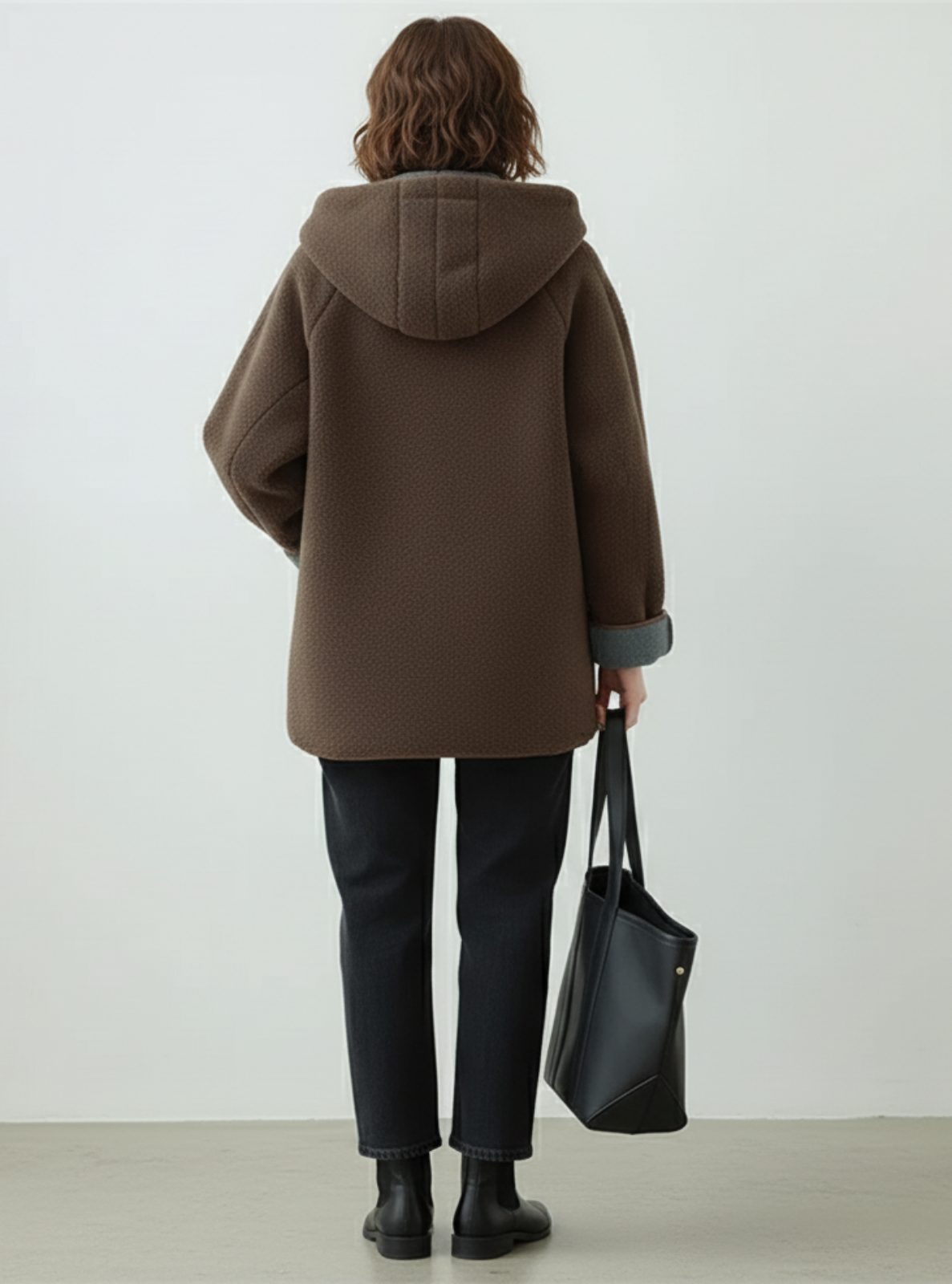 Person wearing a brown coat holding a black bag against a white background