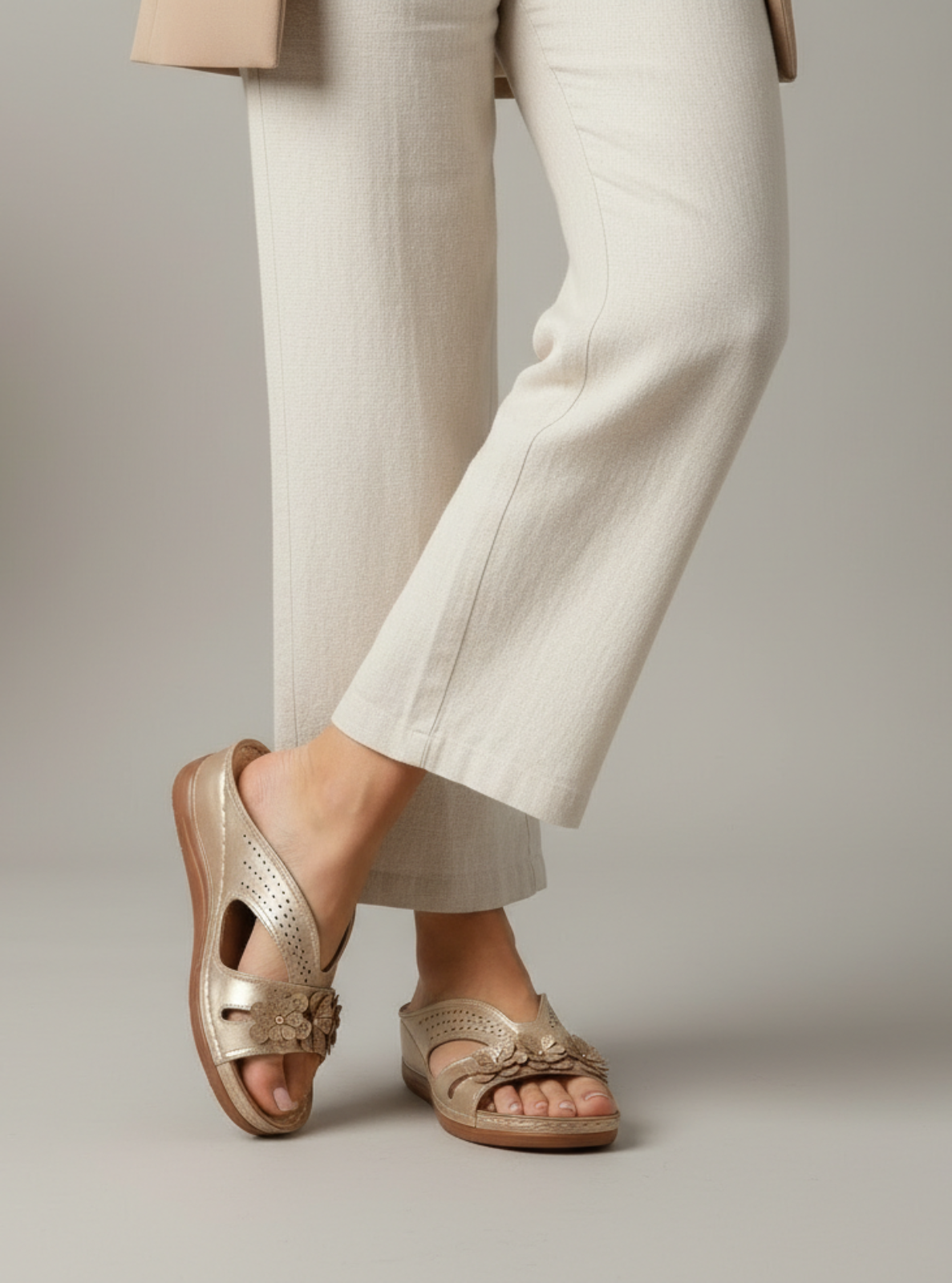Gold sandals worn with light-colored pants on a neutral background