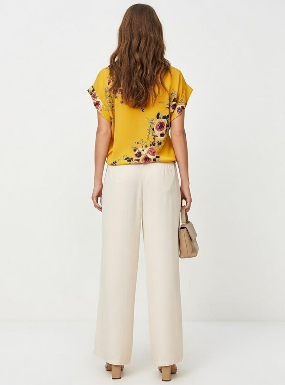 Woman wearing a yellow floral blouse and white pants on a white background