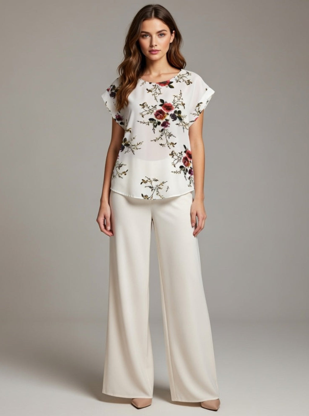 Woman wearing a floral top and white pants on a plain background