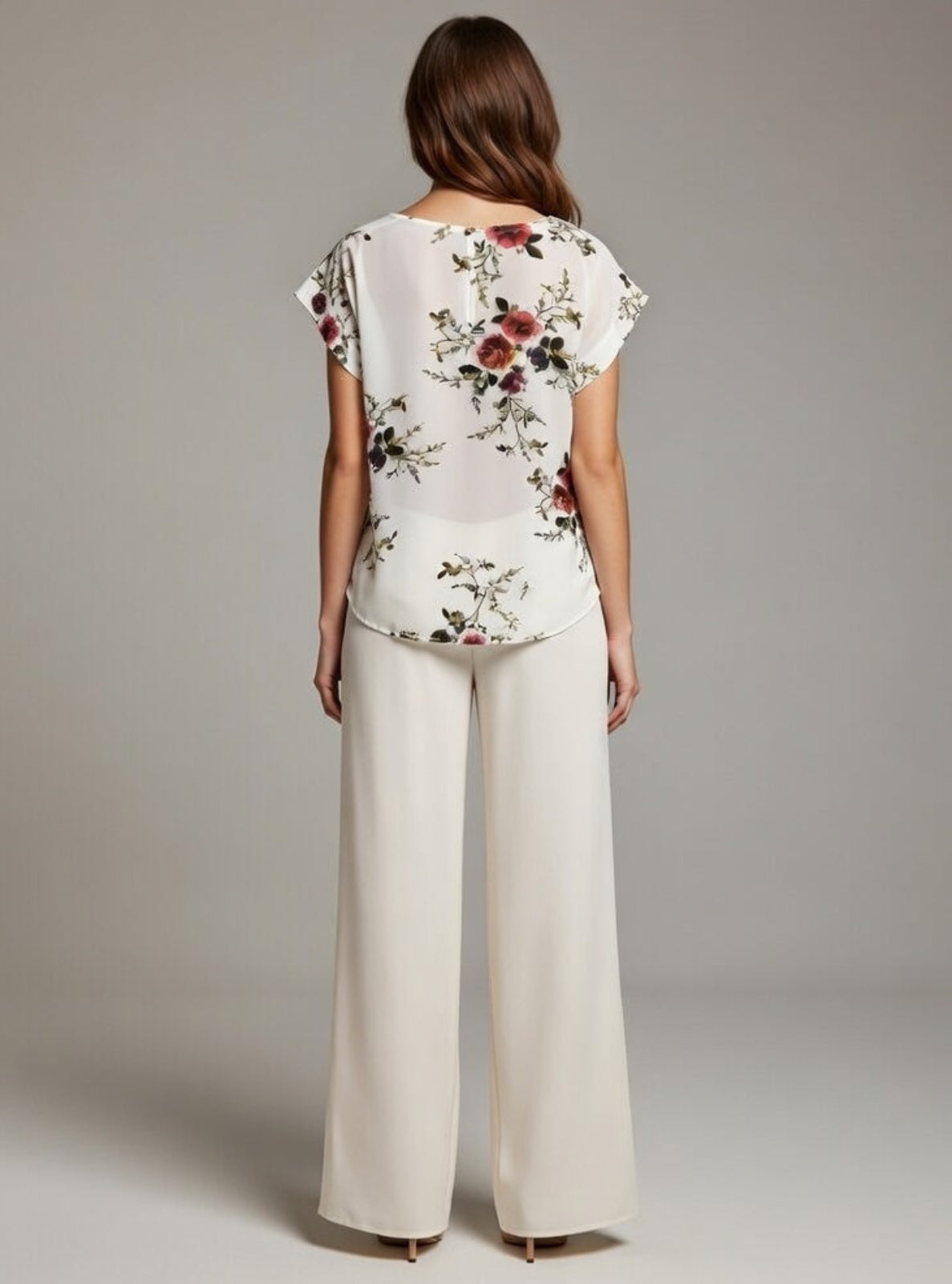 Woman wearing a floral top and white pants against a plain background