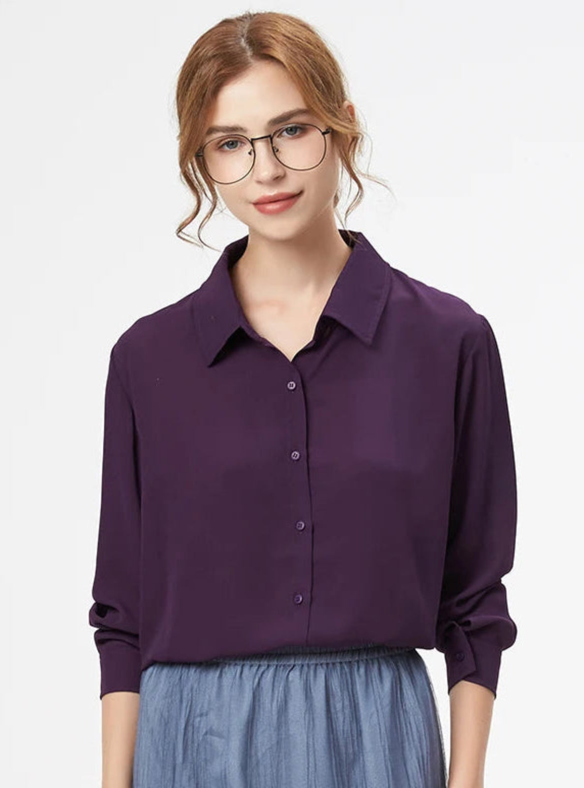 Woman wearing a purple shirt and gray skirt on a light gray background