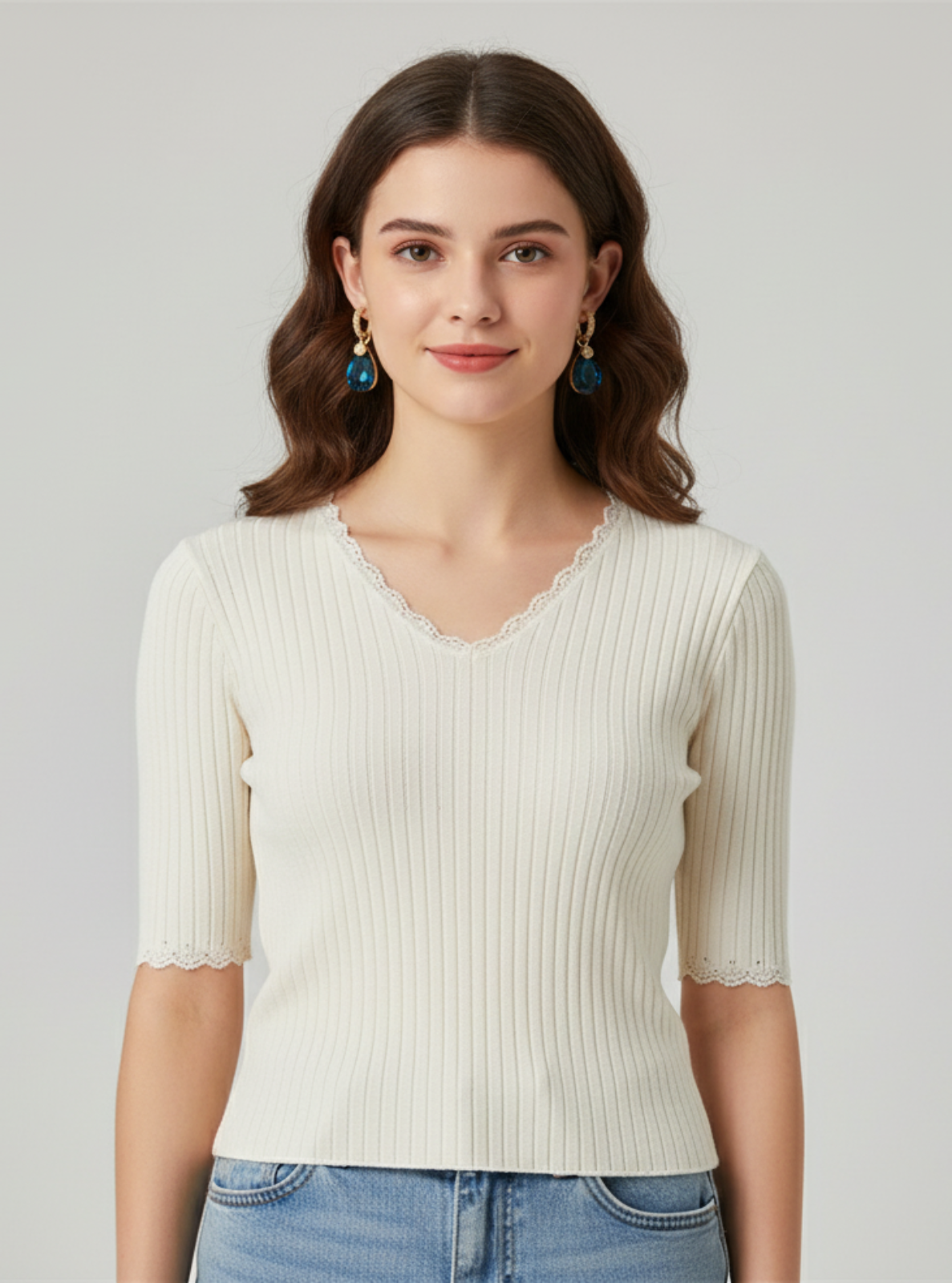 Woman wearing a white ribbed top and blue jeans on a gray background