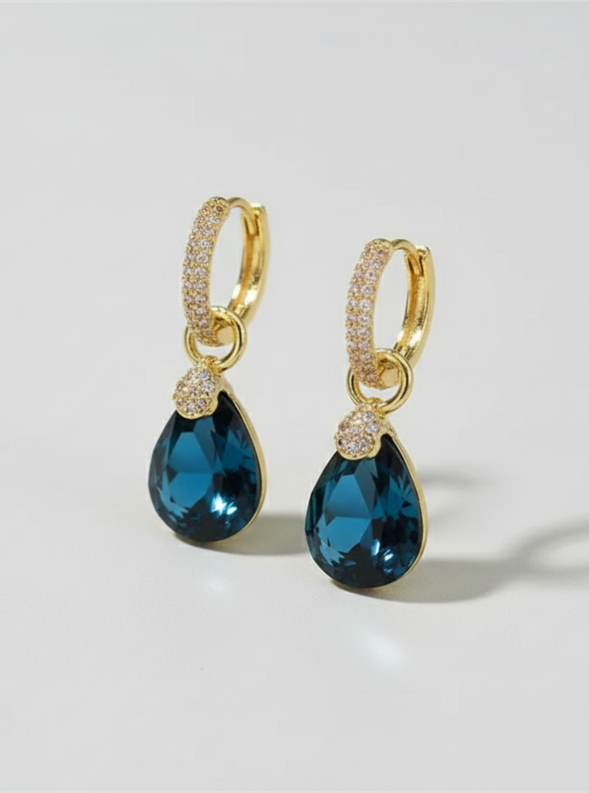 Gold earrings with blue teardrop-shaped gemstones on a light gray background