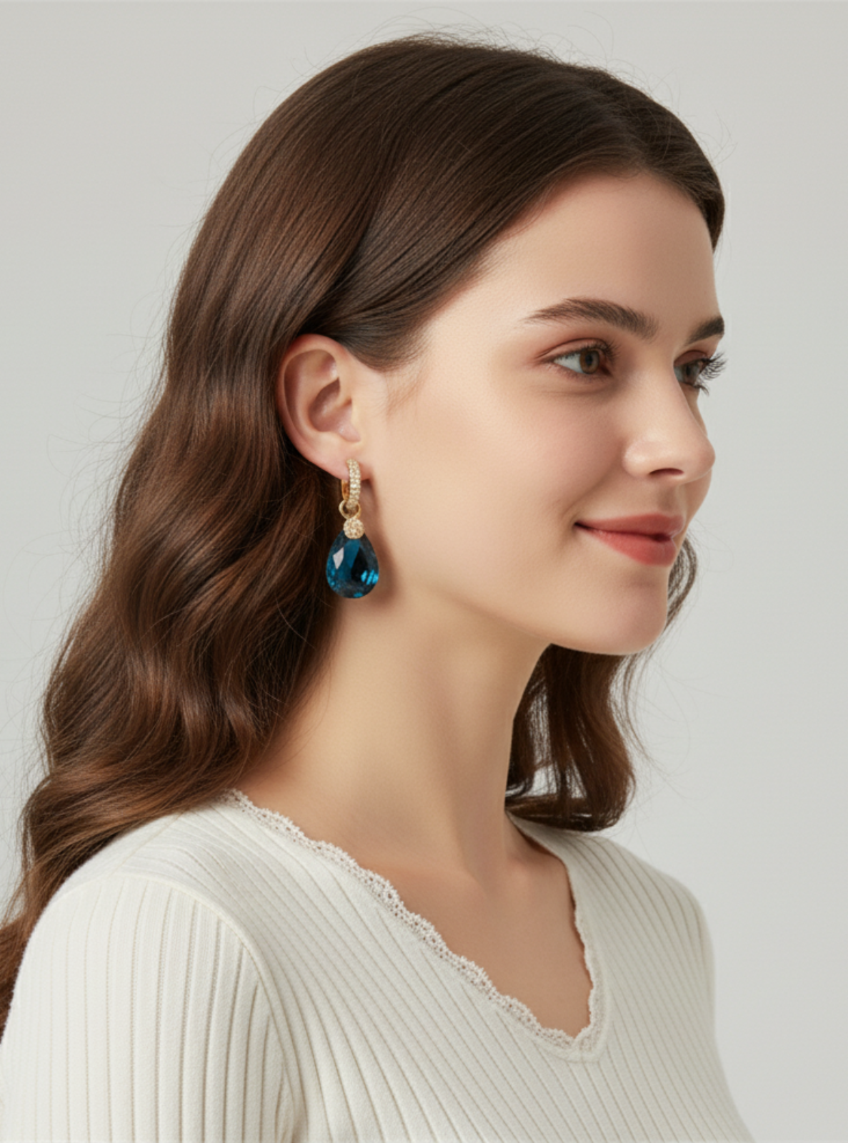 Woman wearing a pair of earrings with a blue gemstone on a plain background