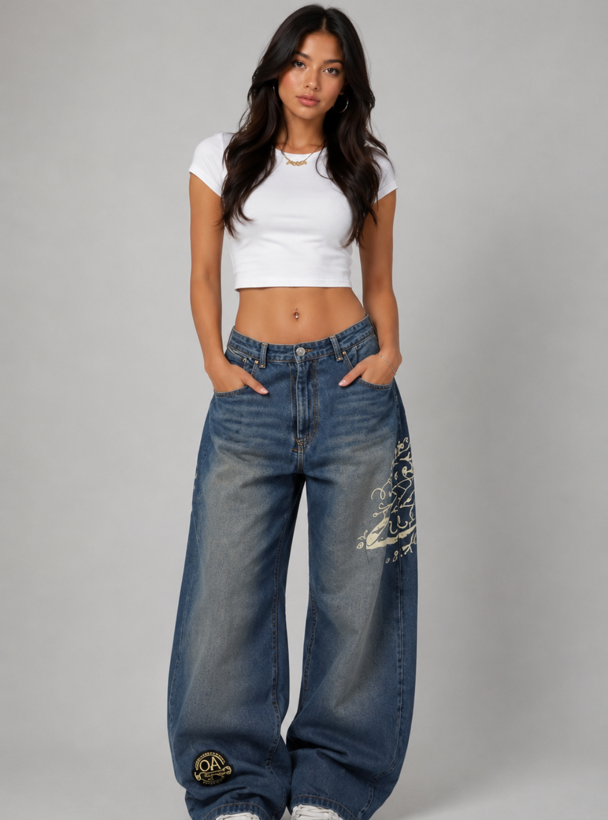 Woman wearing a white crop top and blue jeans with gold designs on a gray background
