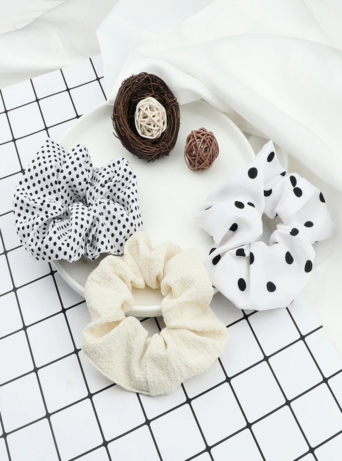 Set of polka dot and plain scrunchies on a white plate with decorative elements.
