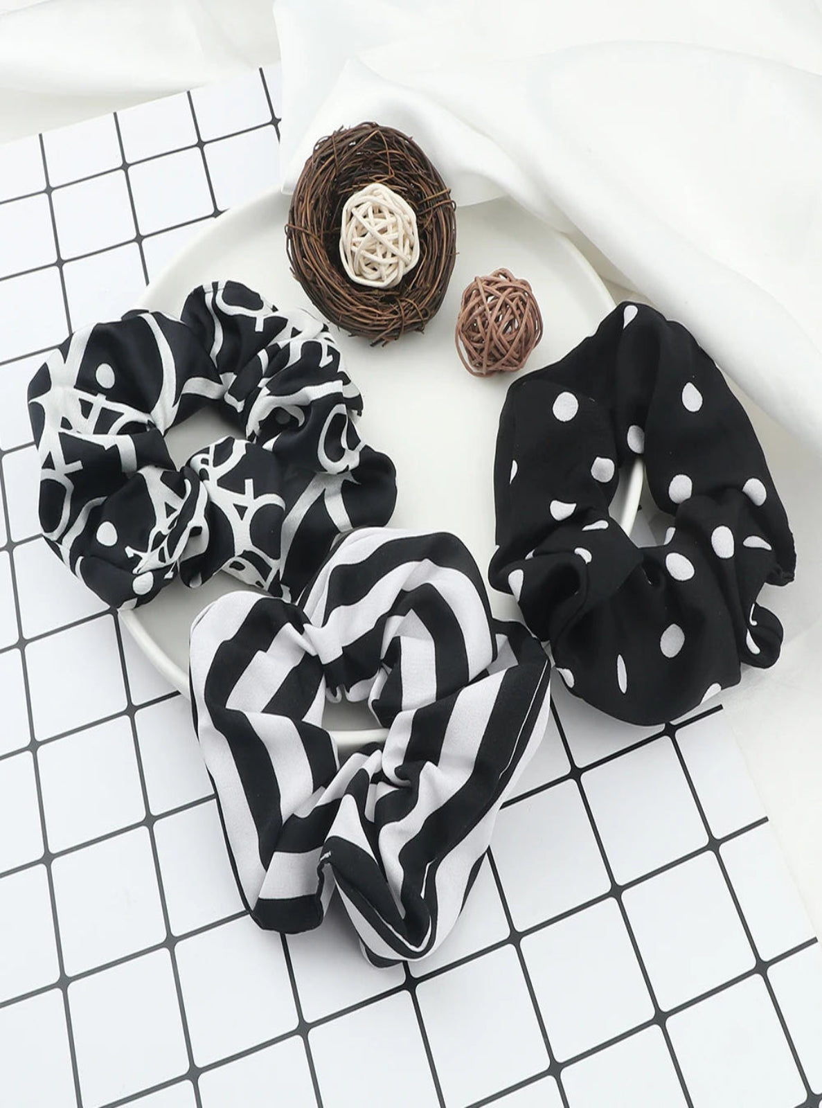 Three black and white patterned scrunchies on a checkered surface with decorative elements.