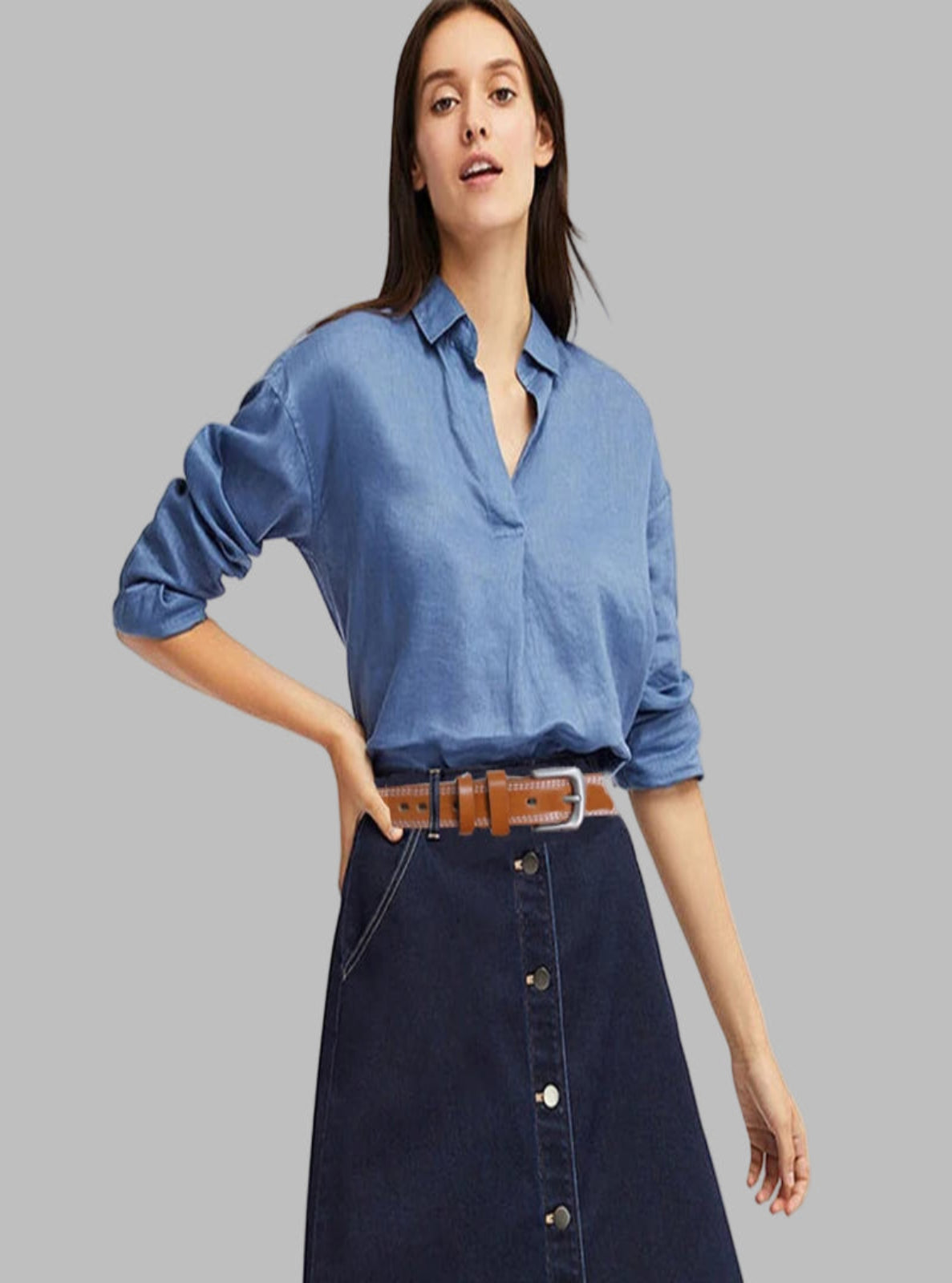 Woman wearing a blue denim shirt and dark denim skirt with a brown leather belt on a white background
