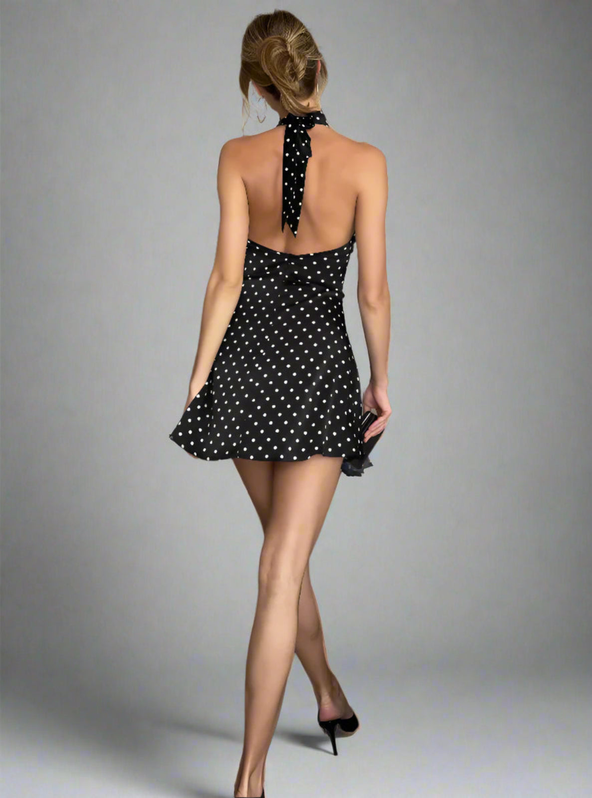 Woman in a black polka dot dress standing in a gray studio setting