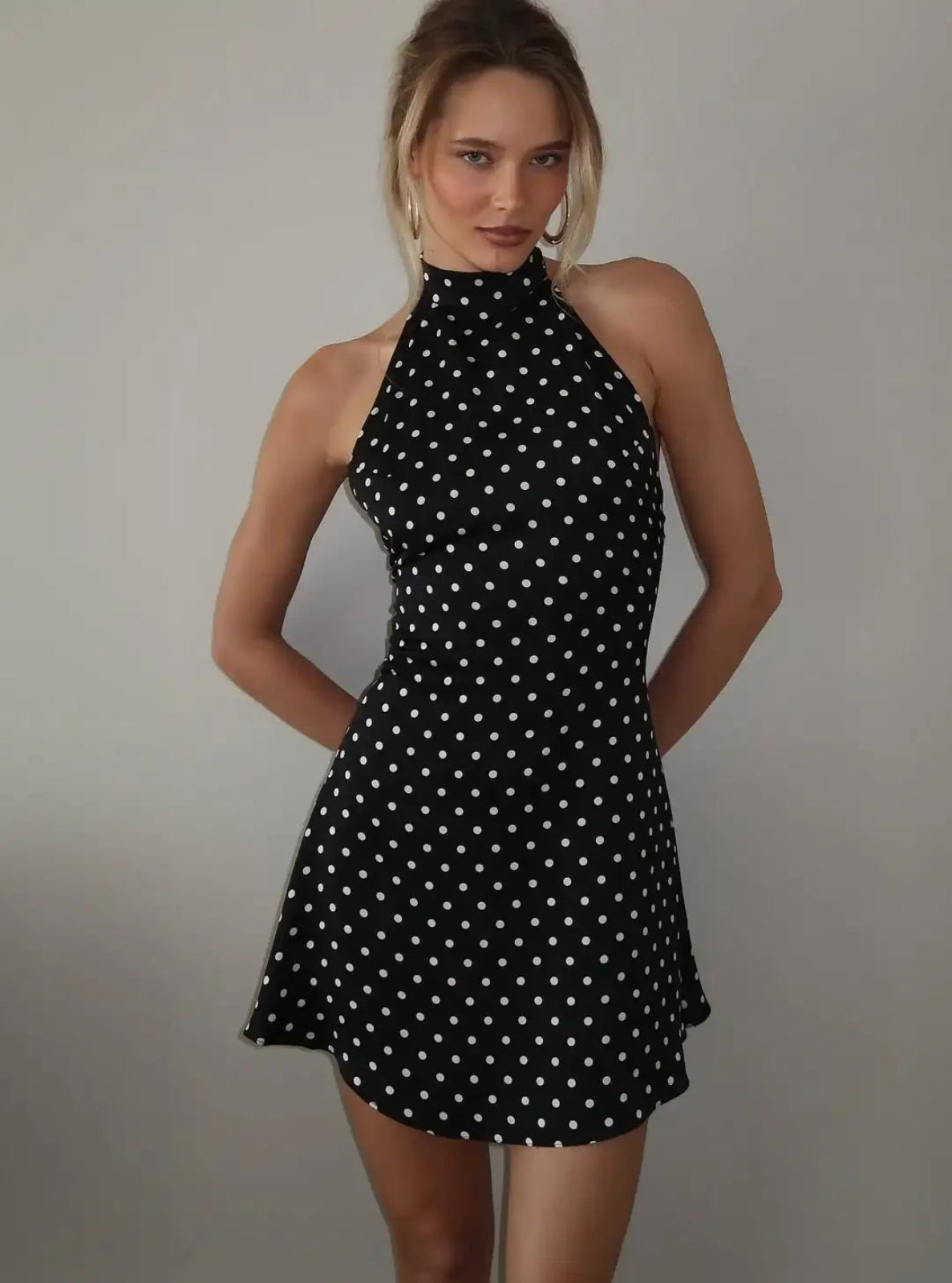 Woman wearing a black dress with white polka dots against a plain background