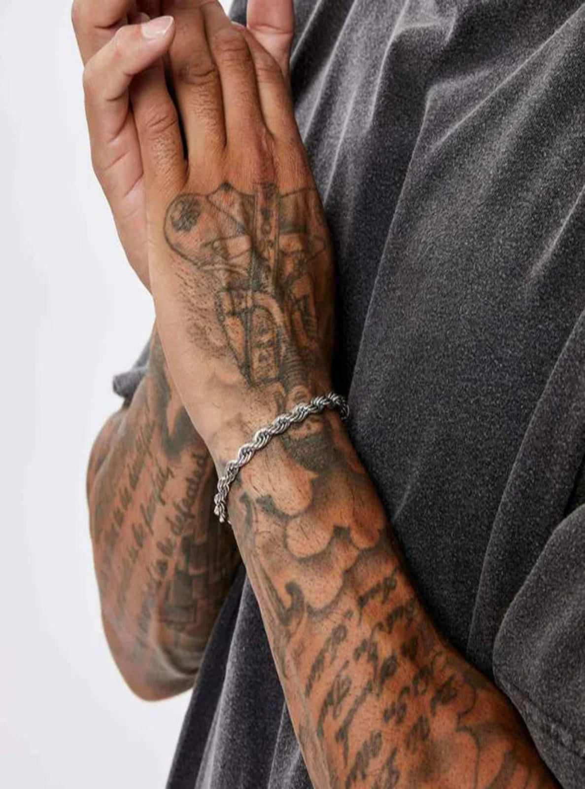 Person with tattooed arms wearing a silver chain bracelet on a plain background