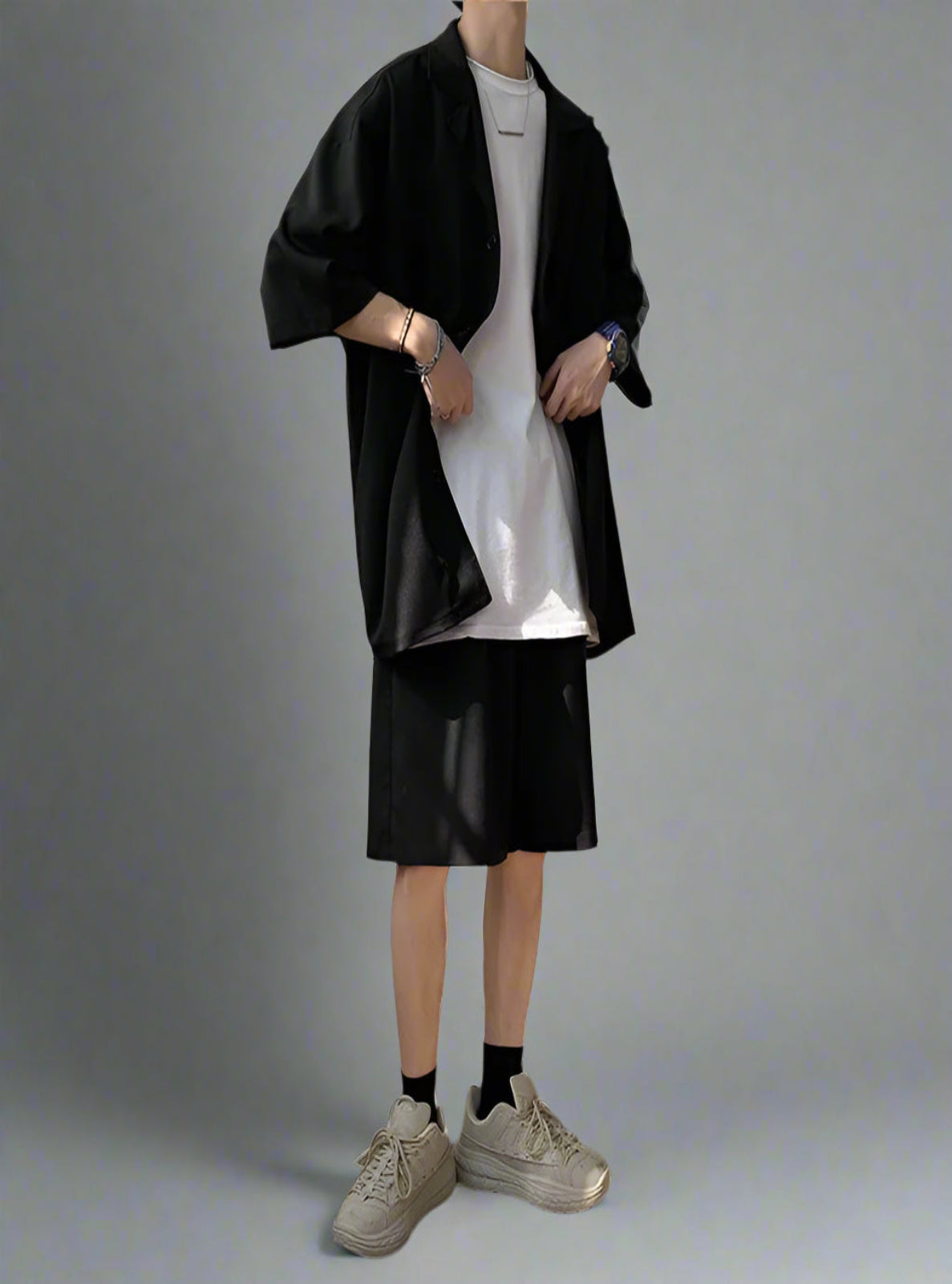 Person wearing a black jacket, white shirt, and black leather shorts in a minimalistic room.