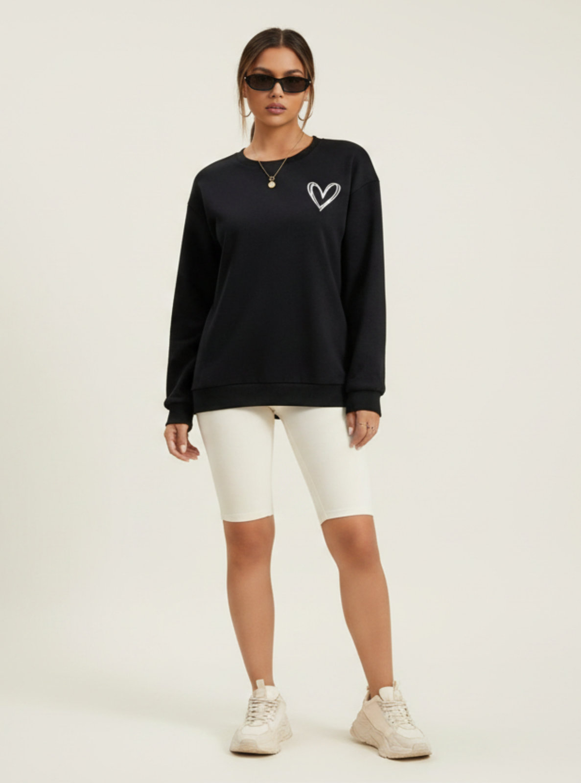 Woman wearing a black sweatshirt with a heart design, white pants, and sneakers on a light background