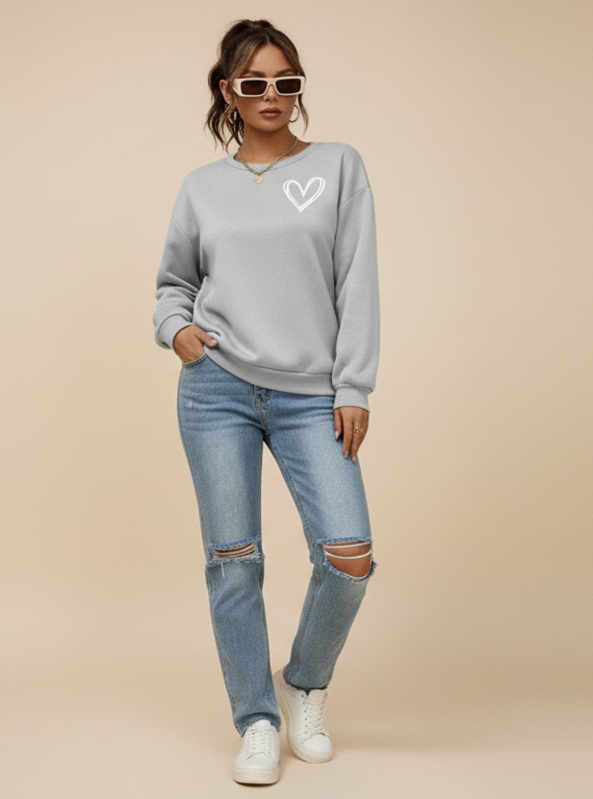 Woman wearing a gray sweatshirt with a heart design and ripped jeans on a beige background