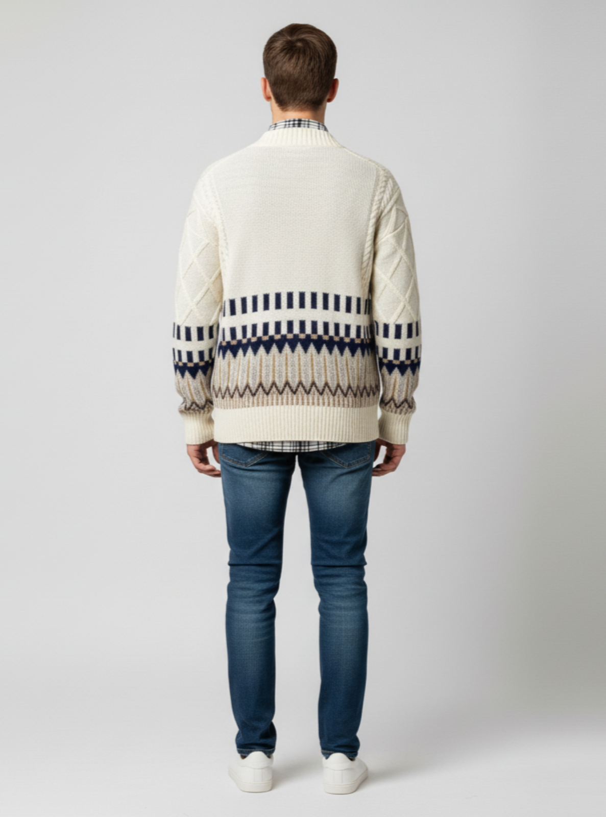 Man wearing a cream sweater with a patterned design on a plain background