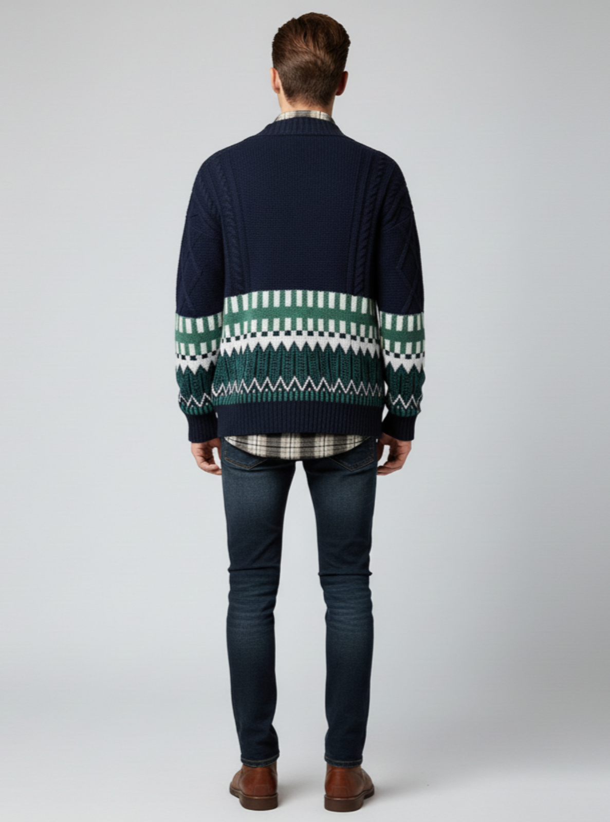 Man wearing a navy sweater with a green and white pattern on a plain background