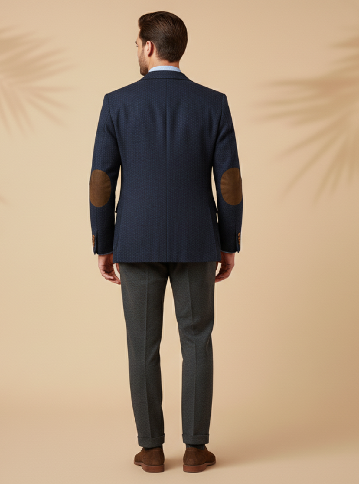 Man wearing a navy blazer with brown elbow patches on a beige background