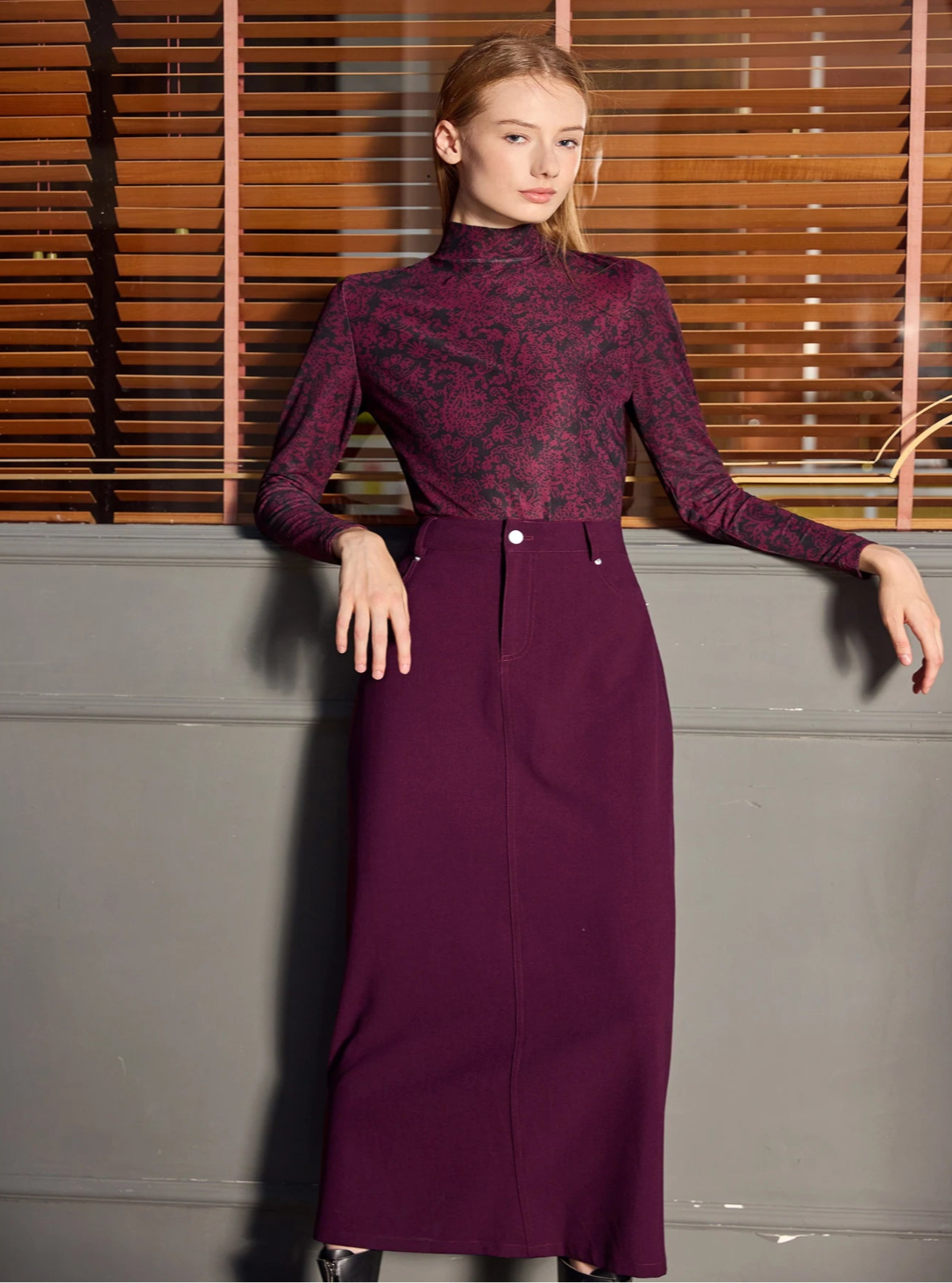 Woman wearing a long purple dress with a patterned top against a neutral background