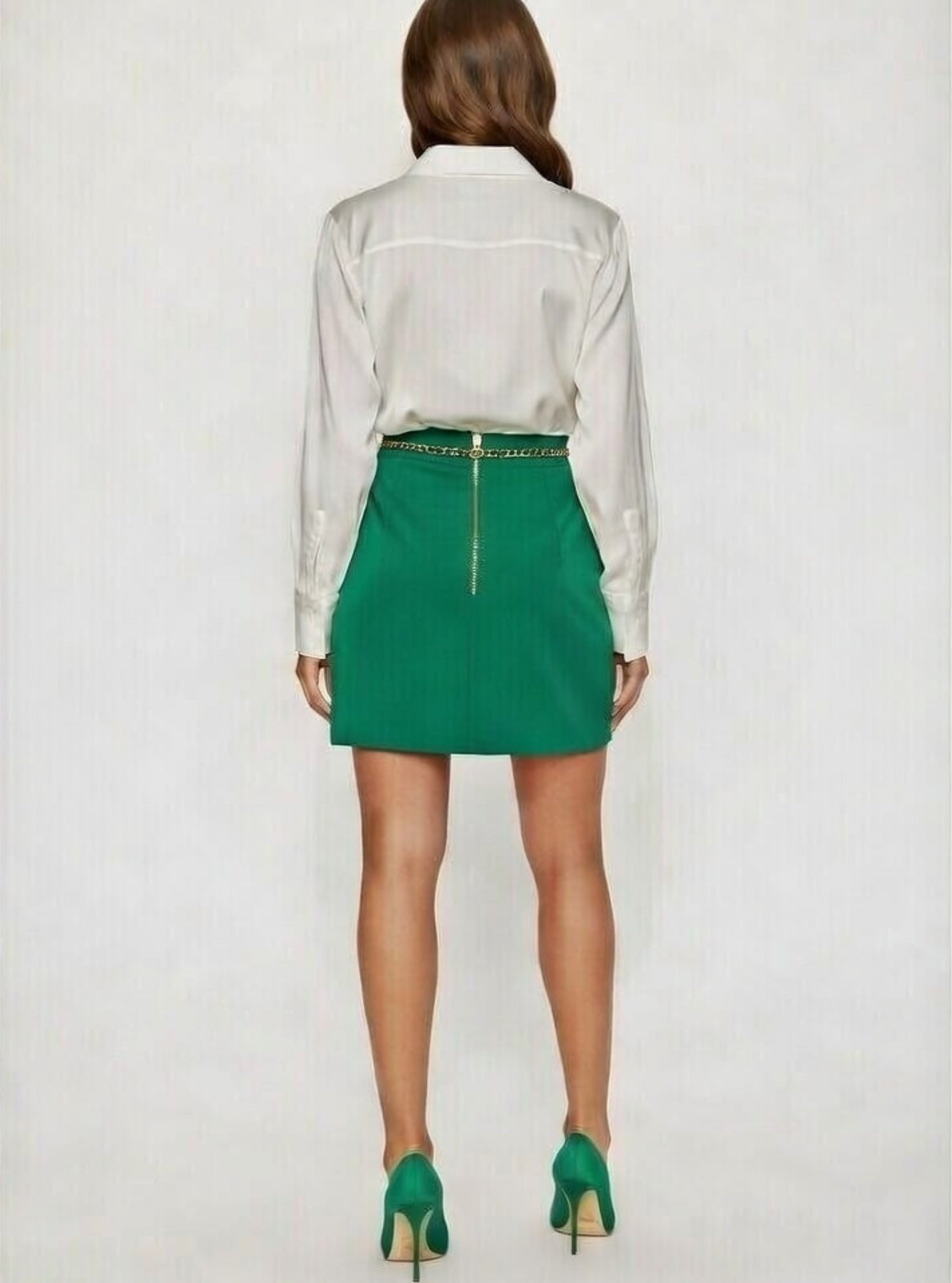 Person wearing a white blouse and green skirt with a gold zipper on a plain background