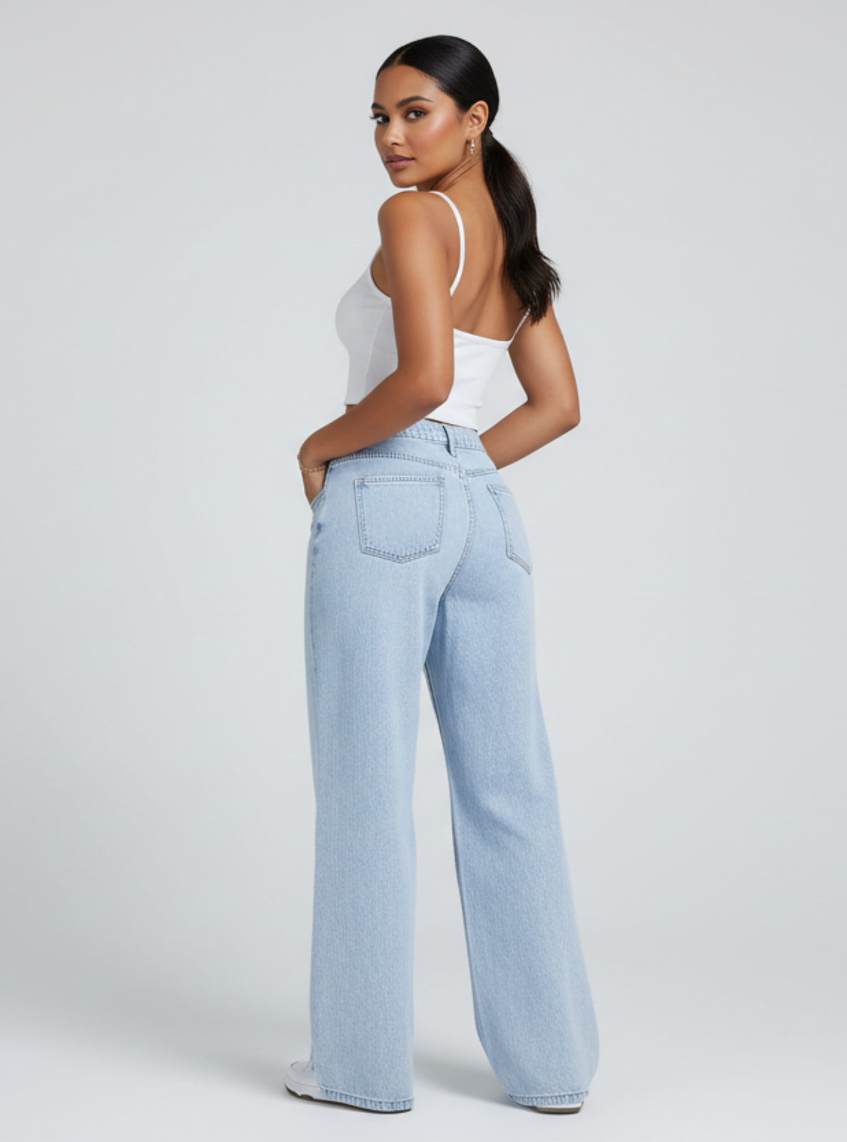 Woman wearing light blue jeans and a white top on a plain background