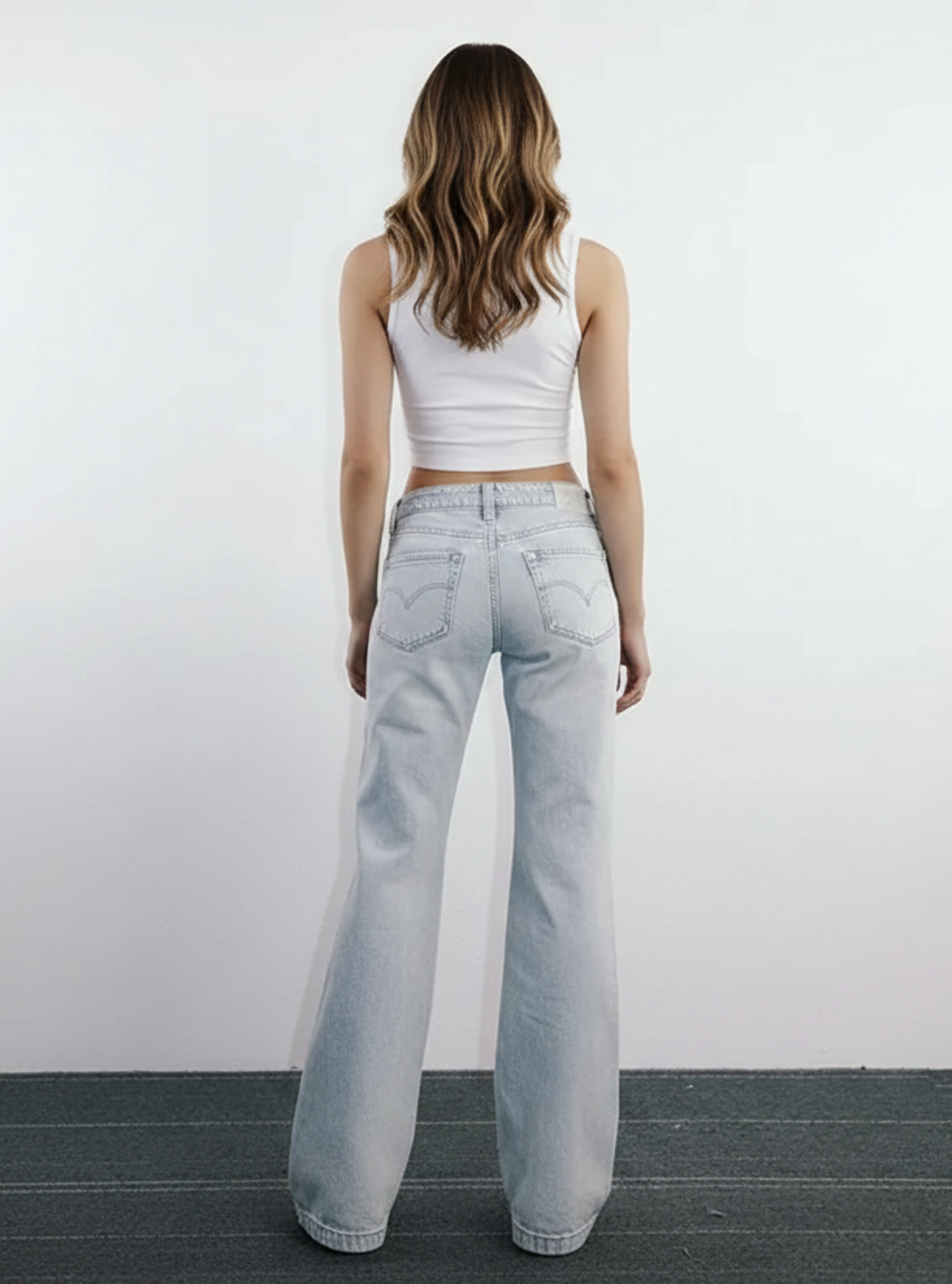 Person wearing light blue jeans and a white top against a plain background