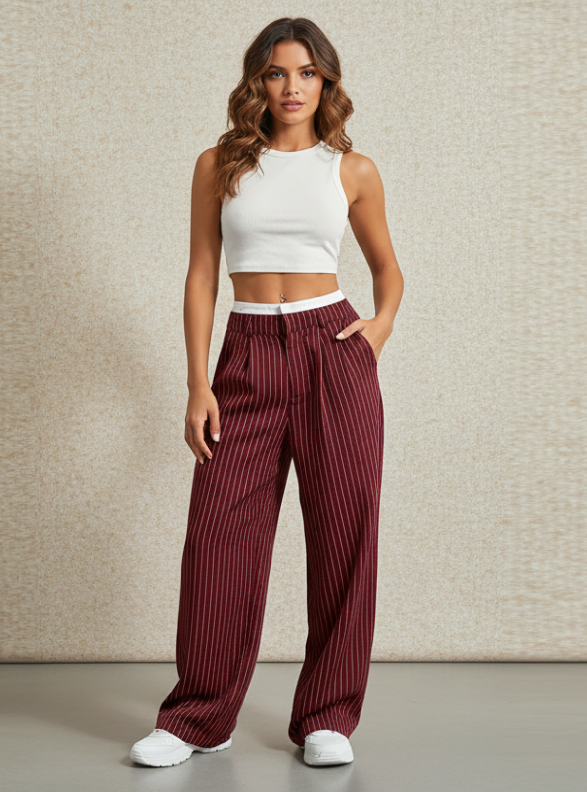Woman wearing a white crop top and maroon striped pants against a beige wall.