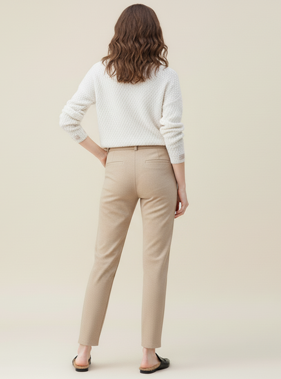 Woman wearing a white sweater and beige pants against a plain background