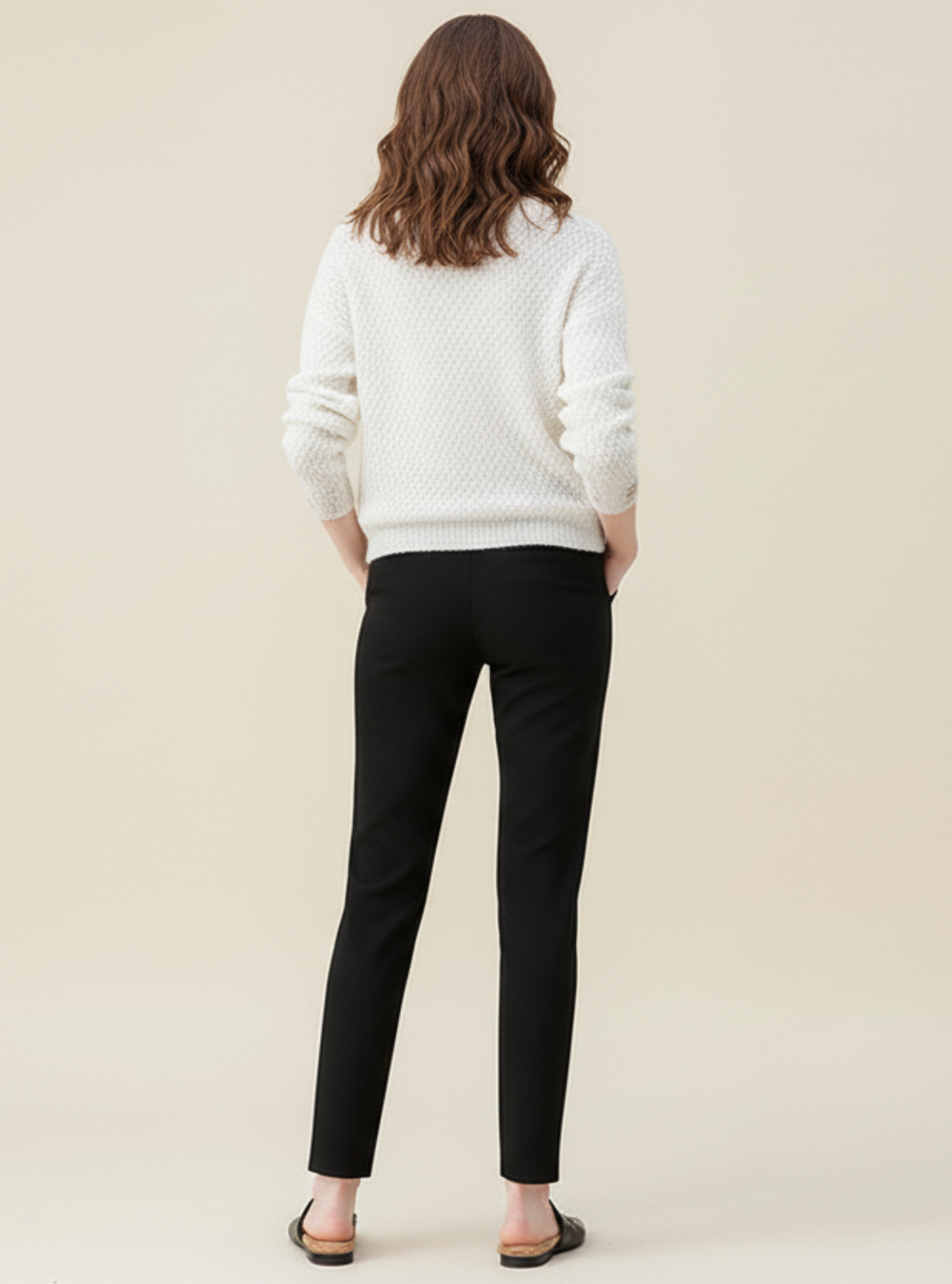 Person wearing a white sweater and black pants against a beige background