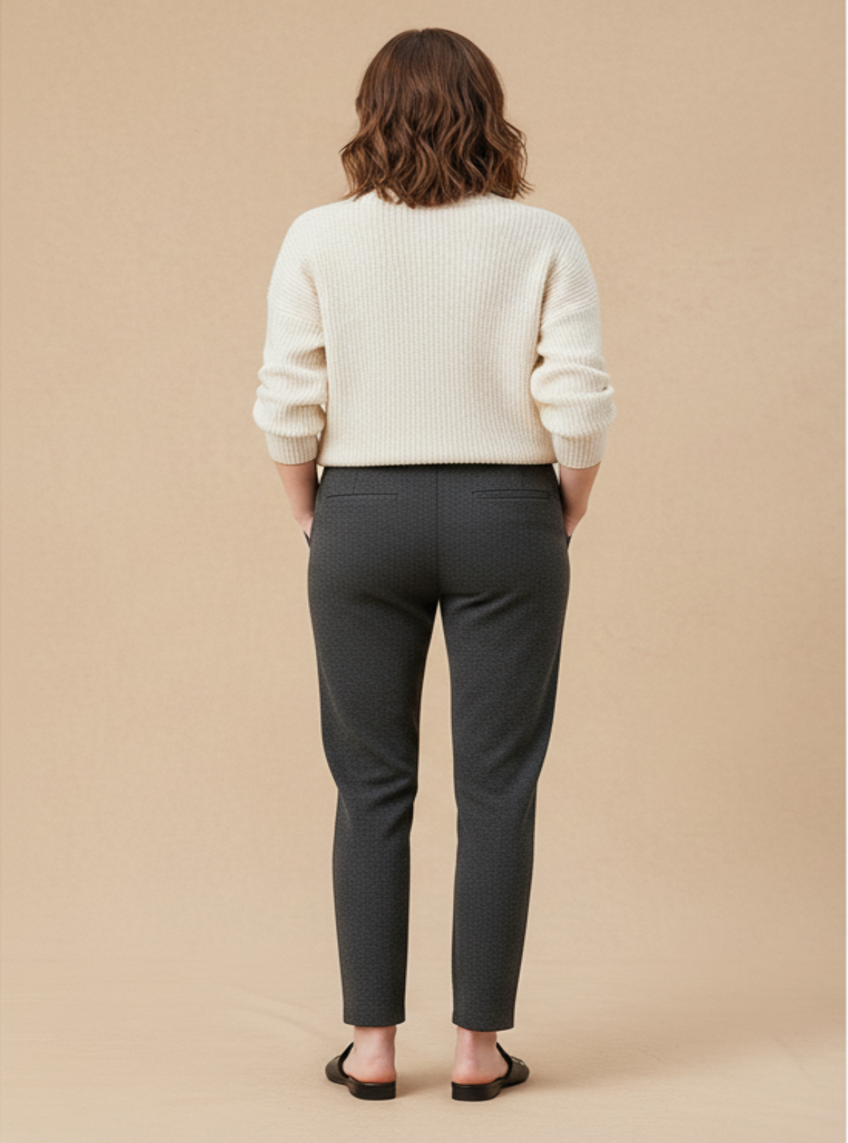 Person wearing a white sweater and dark gray pants against a beige background