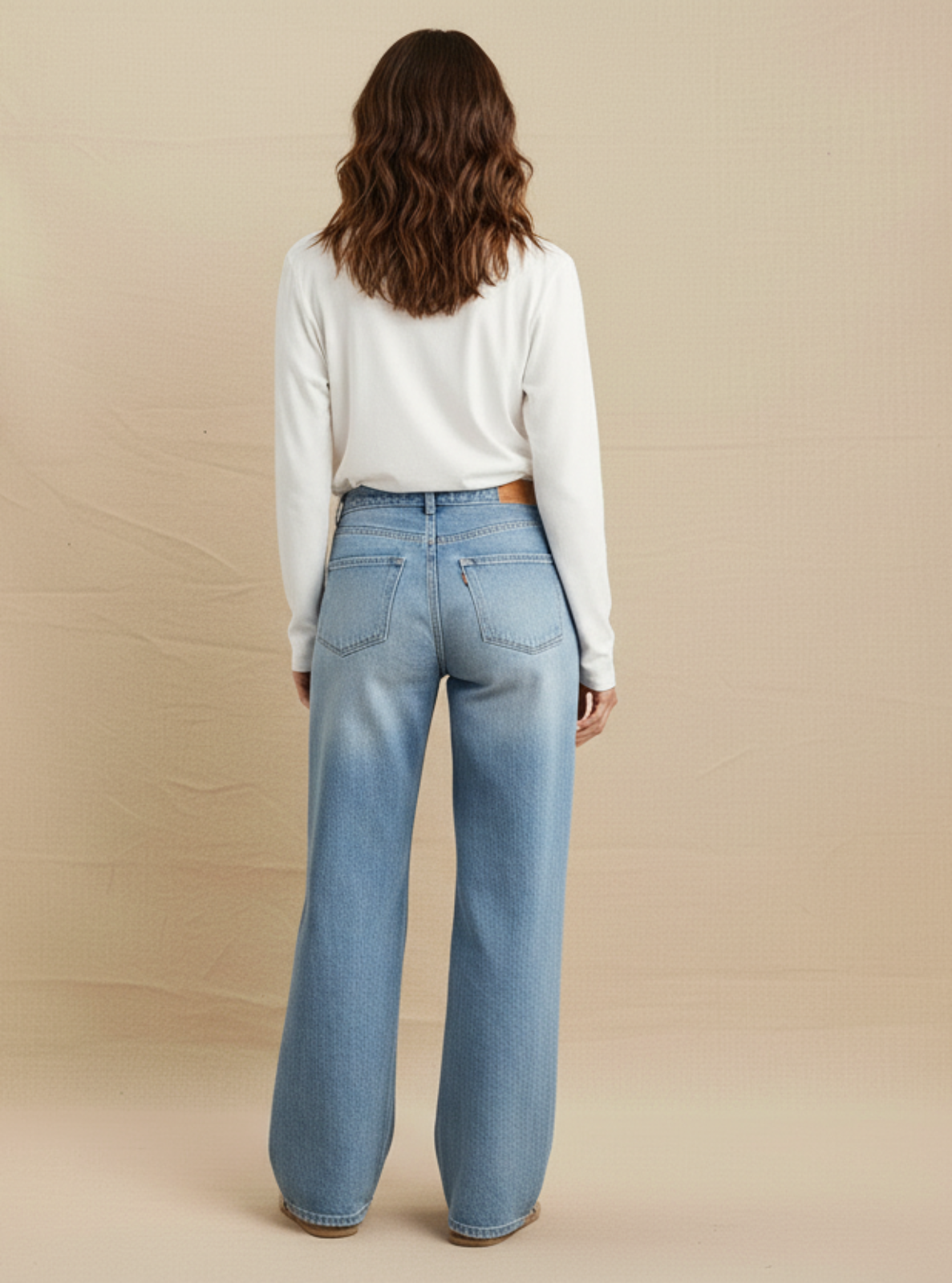 Woman wearing light blue jeans and a white top on a beige background