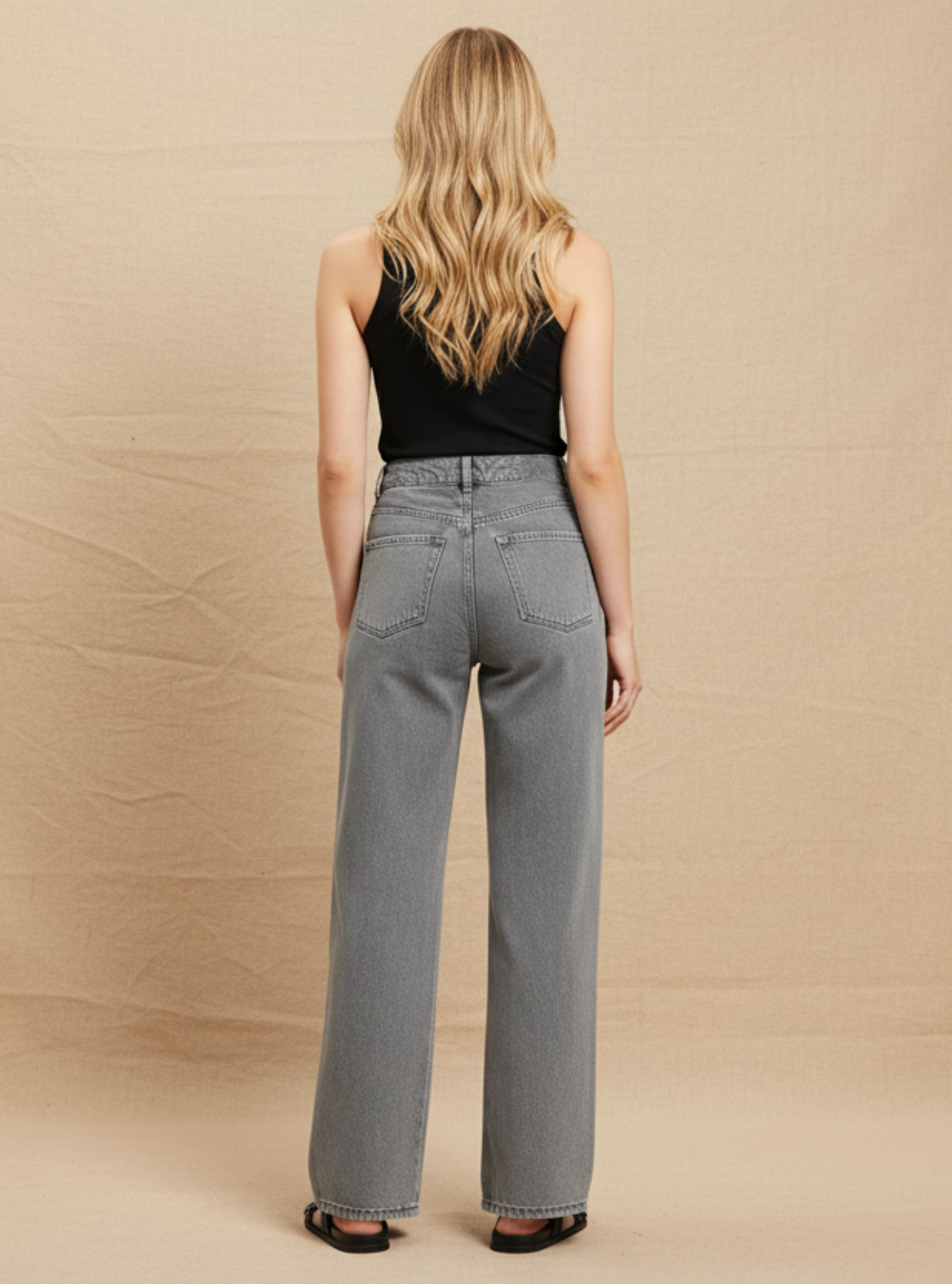 Woman wearing gray pants and a black top standing against a beige background