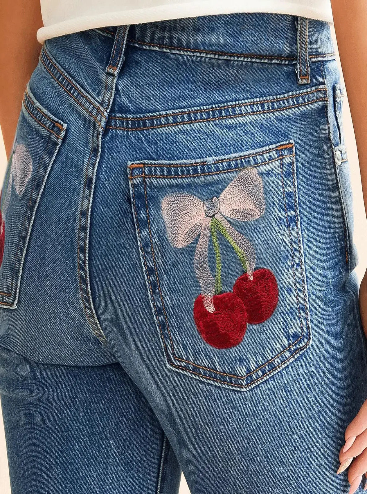 Blue jeans with a decorative pocket featuring a bow and cherries.