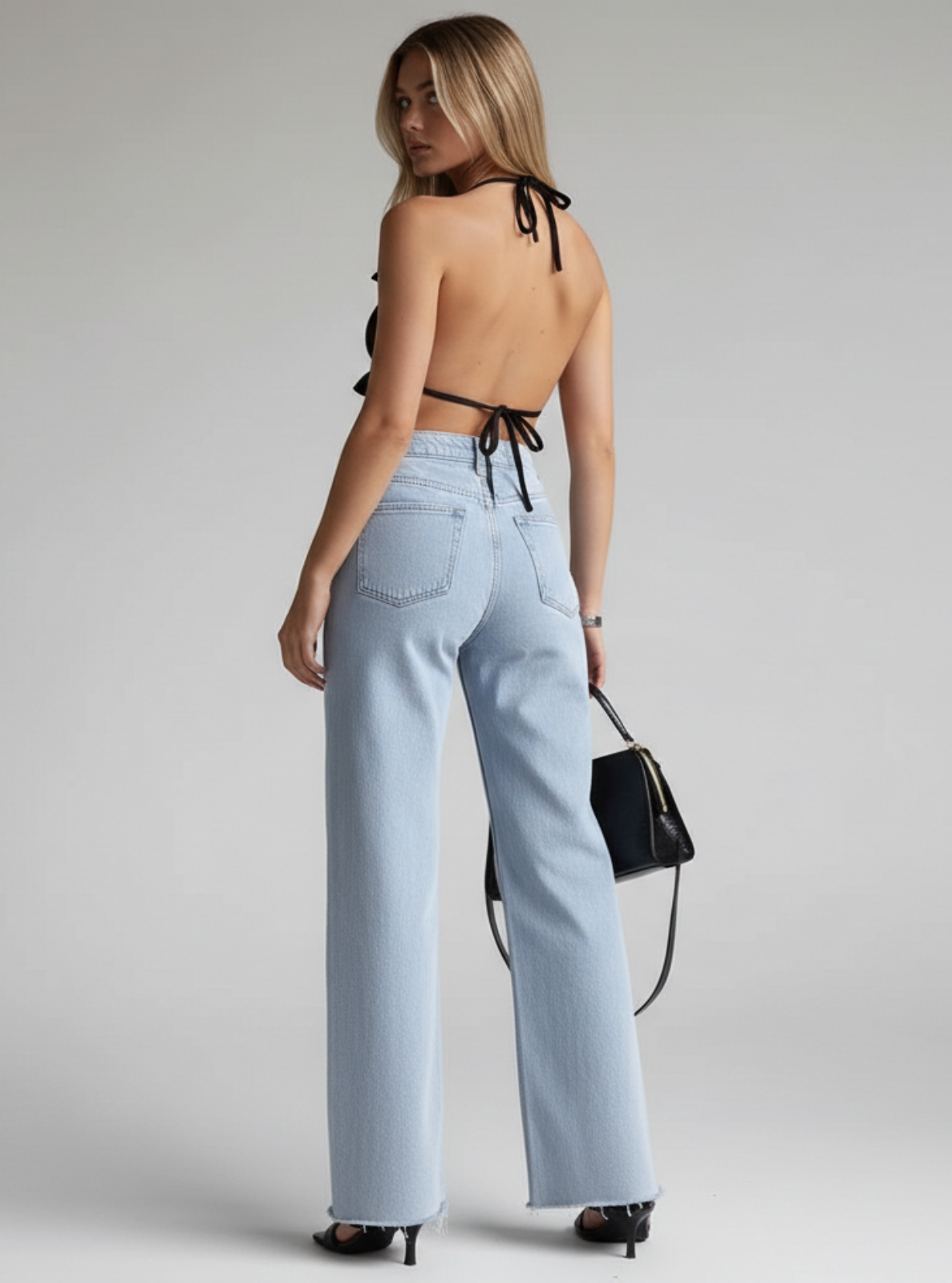 Woman wearing light blue jeans and a black top with thin straps on a gray background