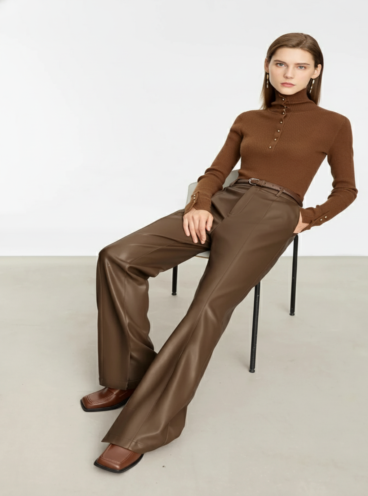 Woman wearing a brown turtleneck and pants sitting on a chair against a white background