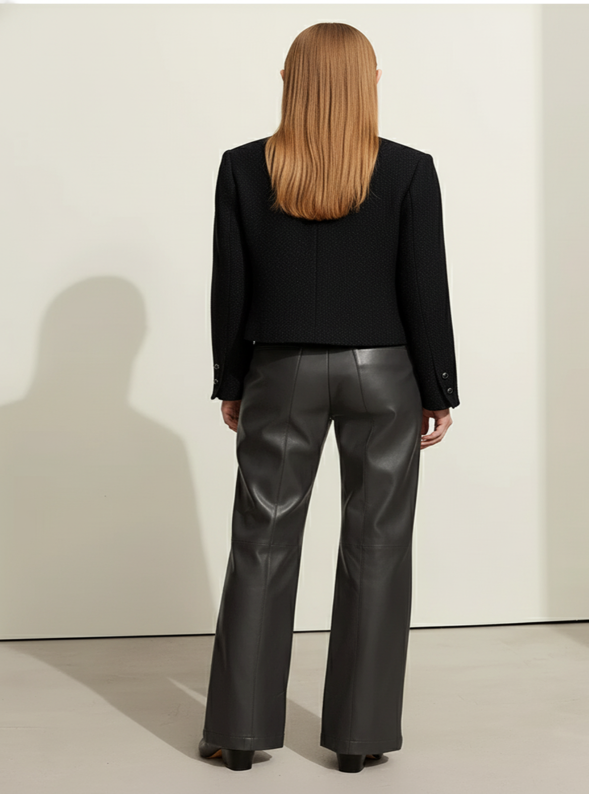 Person wearing a black blazer and dark gray flared pants against a white background