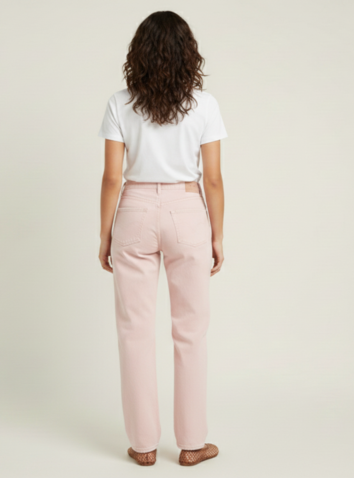 Woman wearing a white top and light pink pants on a beige background