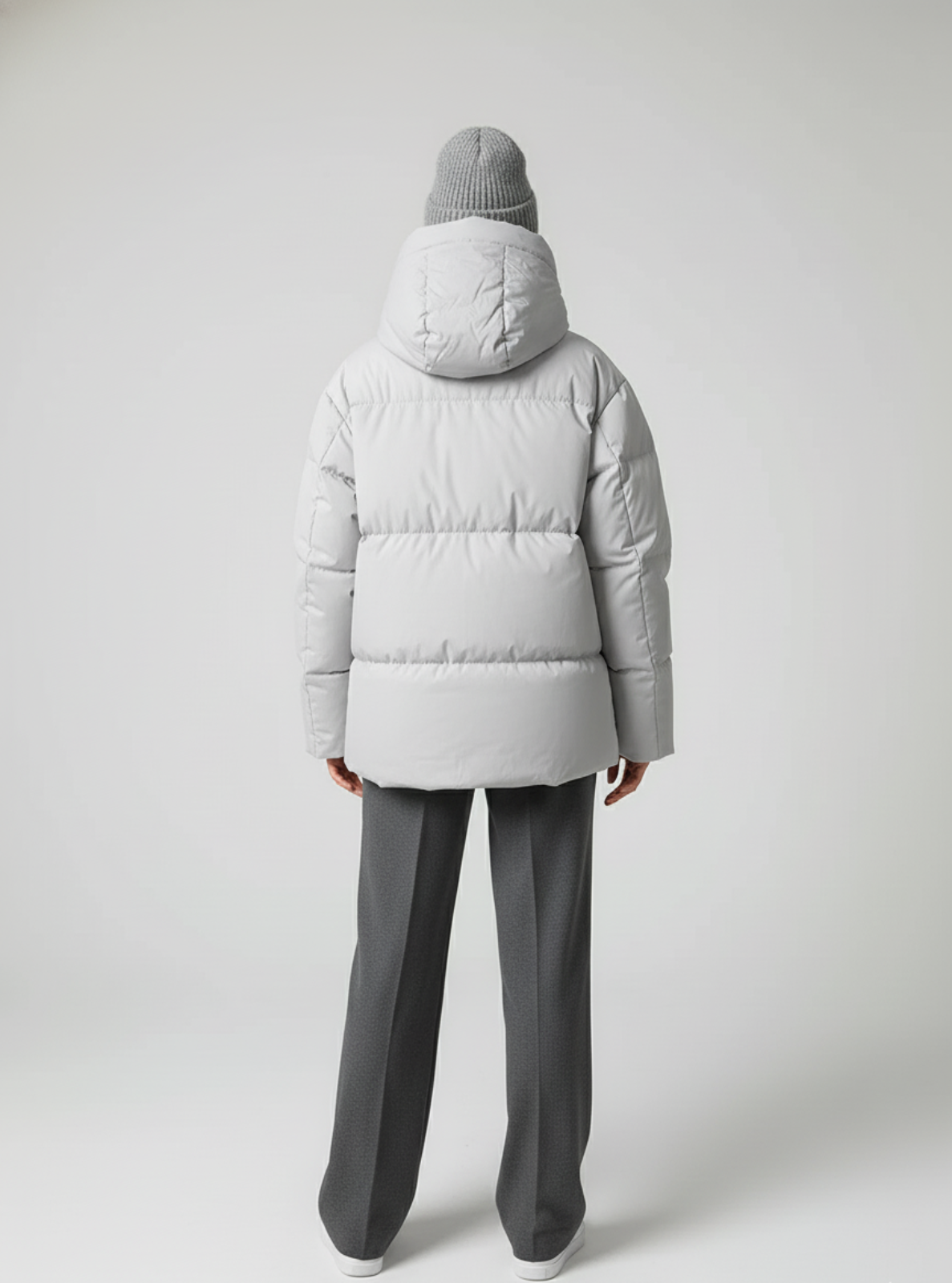 Person wearing a gray puffer jacket and pants on a white background