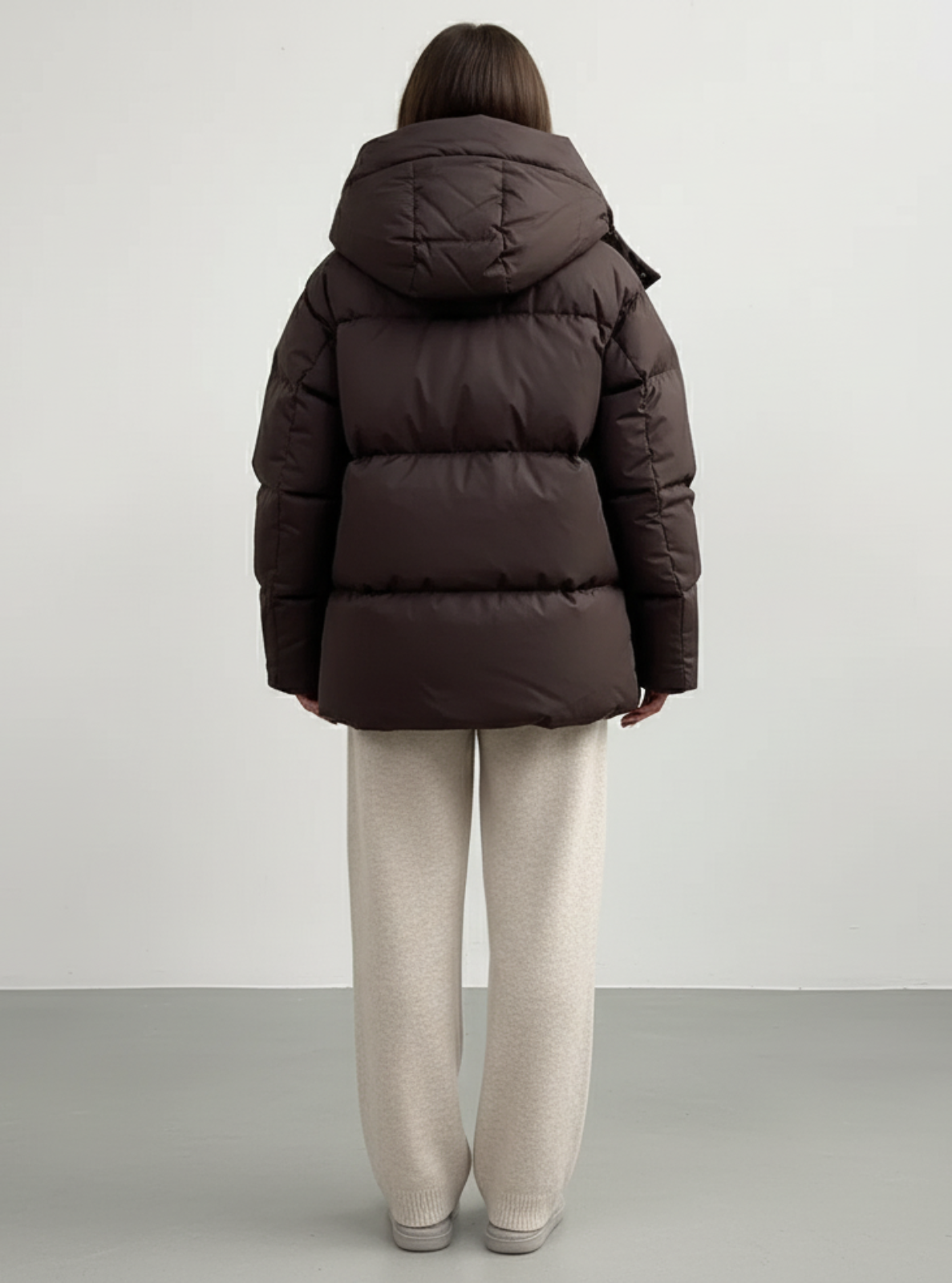 Person wearing a brown puffer jacket and beige pants on a plain background