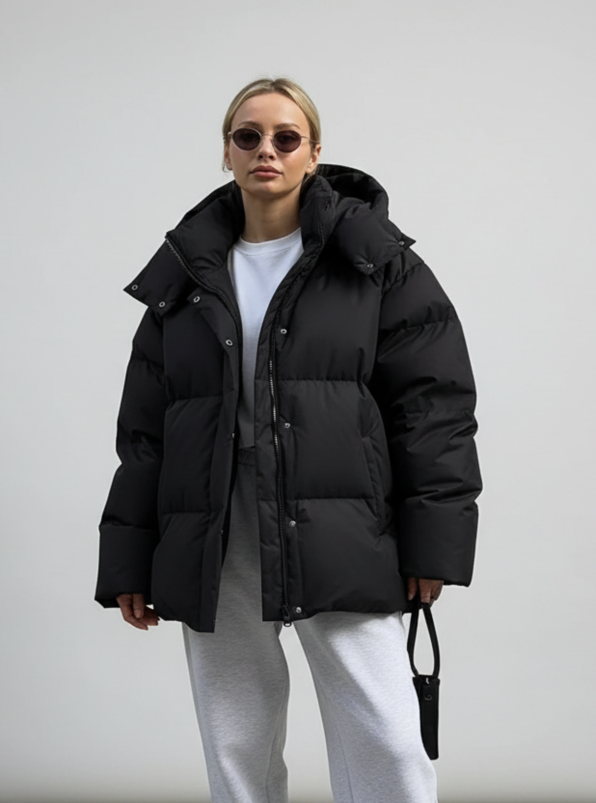 Person wearing a black puffer jacket, white shirt, and light gray pants against a plain background