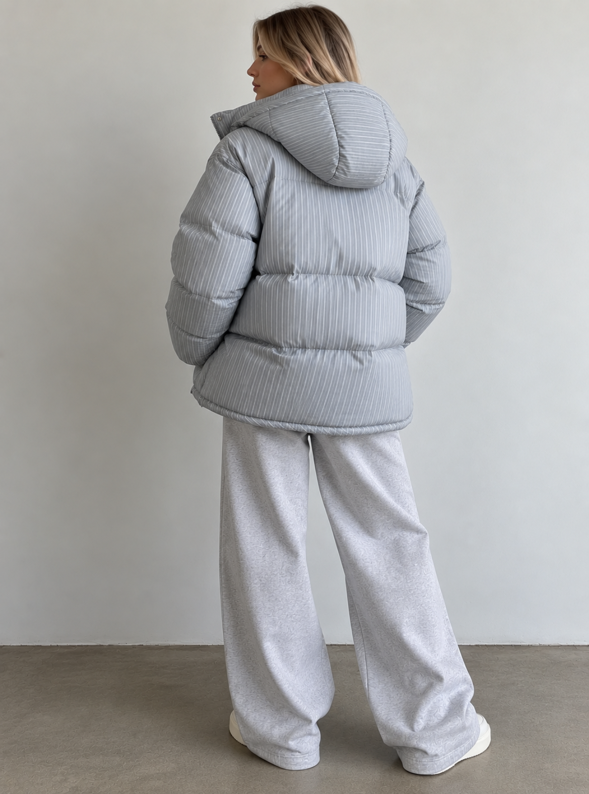 A woman shown from the back wearing a light gray ribbed puffer jacket and matching light gray wide-leg sweatpants, standing against a plain light gray wall.