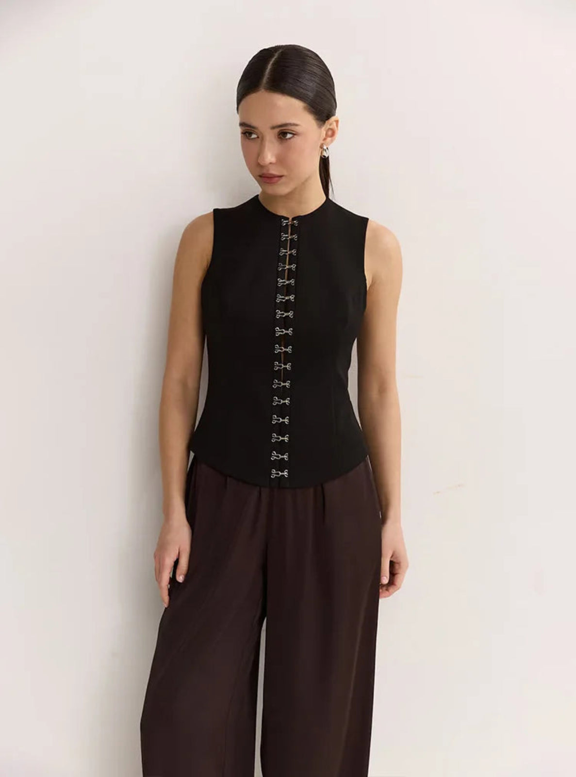 Woman wearing a black sleeveless top with lace-up front and brown pants on a white background