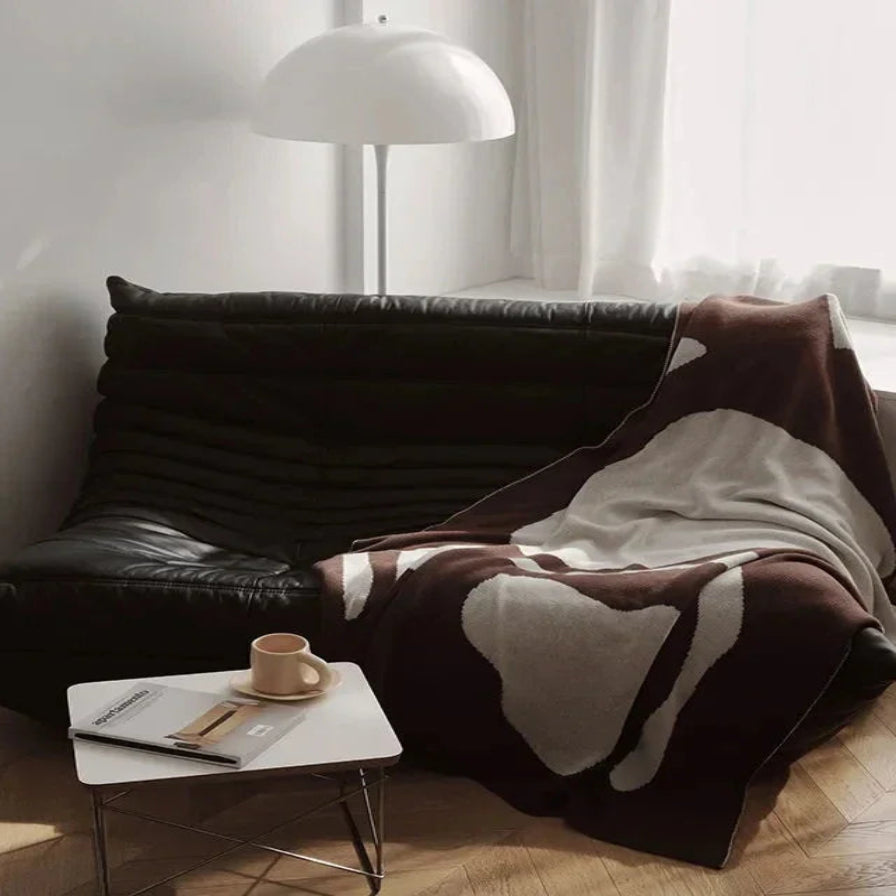 Cozy living room corner with a black leather sofa, cowhide rug, and small table with a mug and book.