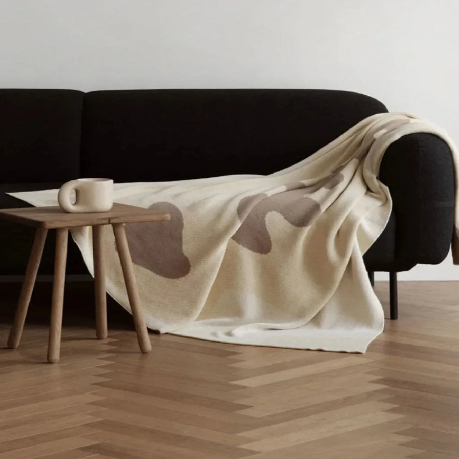 Beige blanket draped over a black sofa with a wooden side table in a minimalistic room.