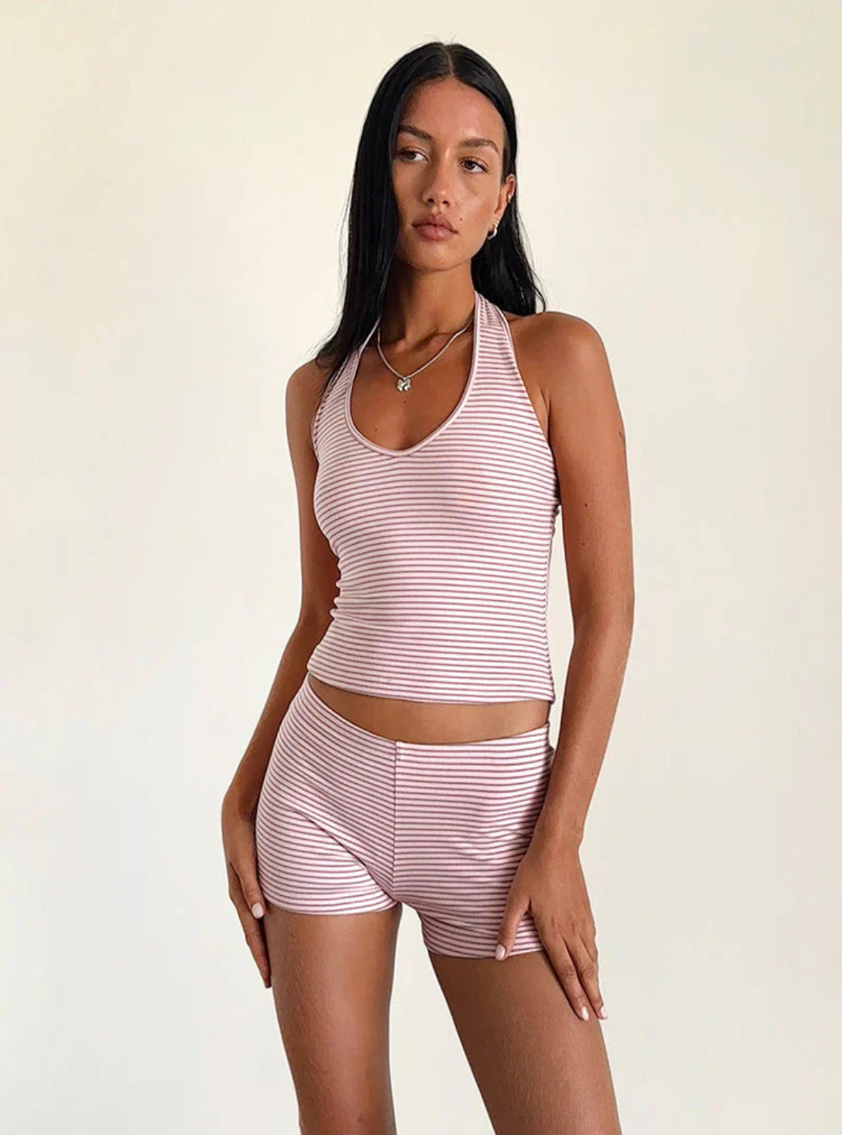 Woman wearing a matching pink and white striped tank top and shorts set on a beige background