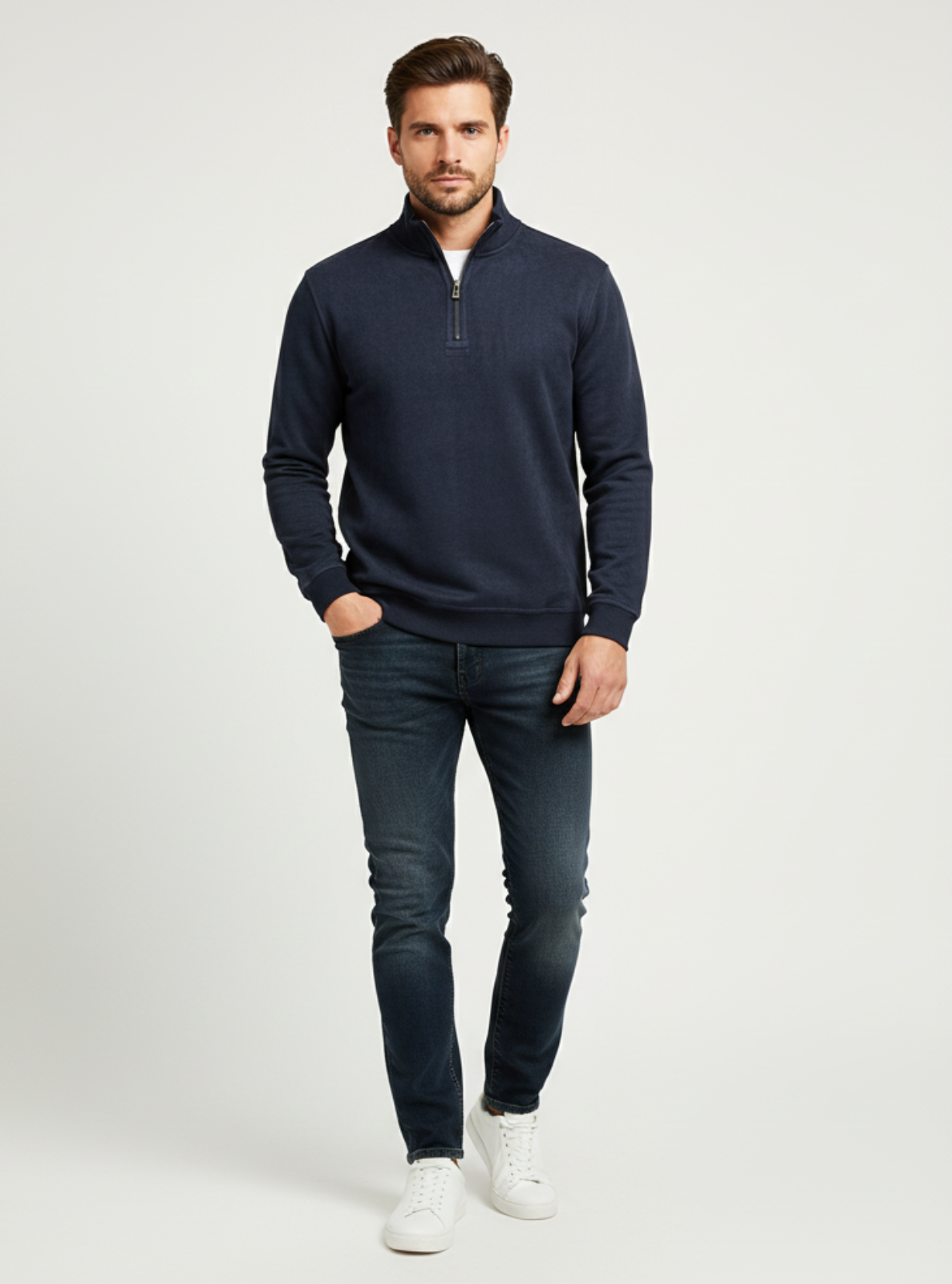 Man wearing a navy half-zip sweater and dark jeans on a light gray background