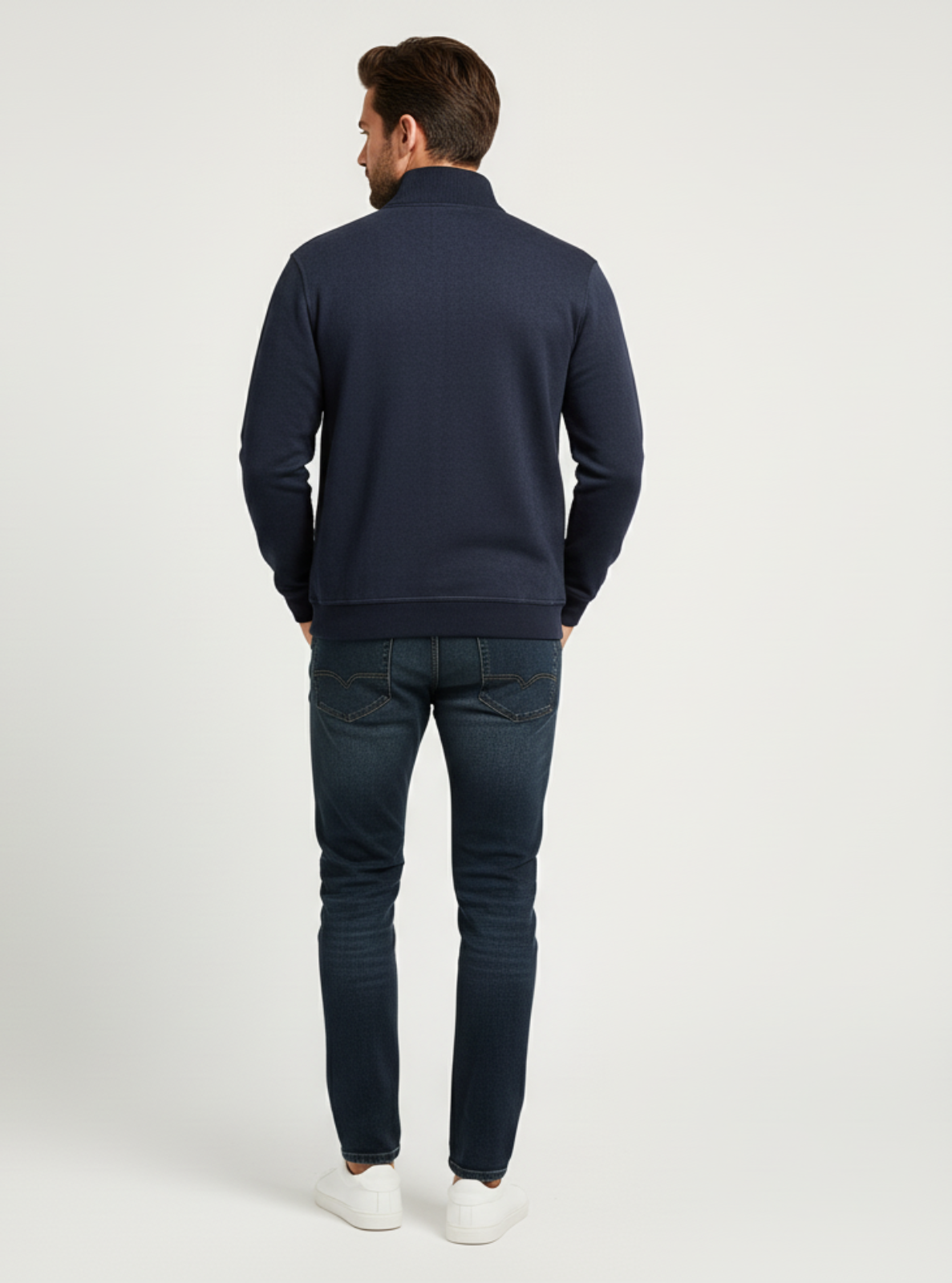 Man wearing a navy sweater and jeans on a white background