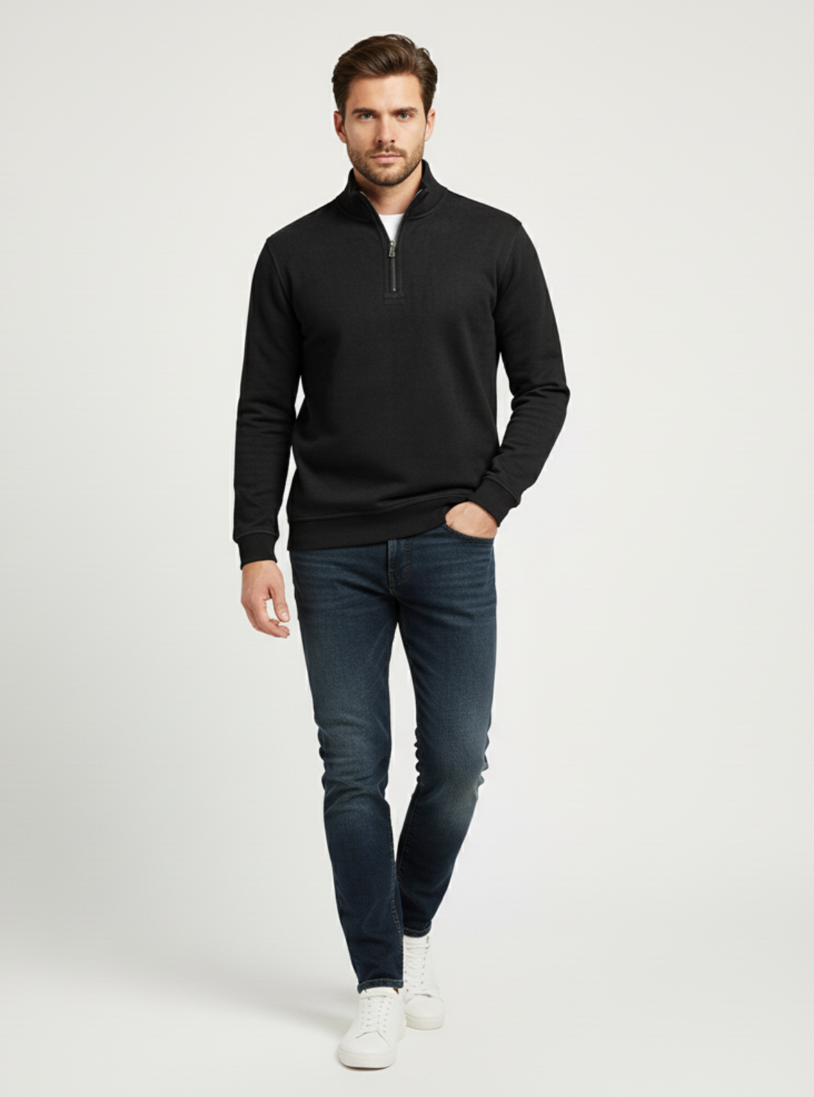 Man wearing a black quarter-zip sweater and blue jeans on a white background