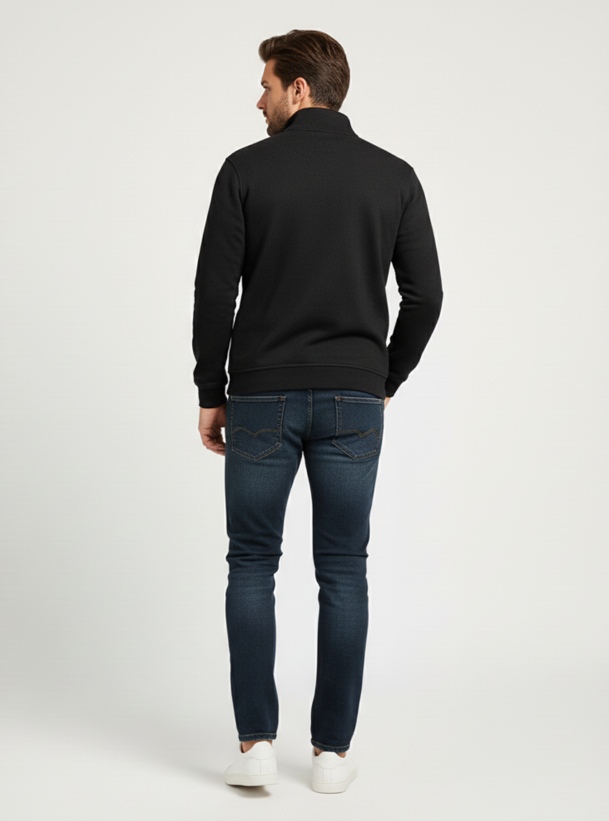 Man wearing a black sweater and dark jeans on a white background