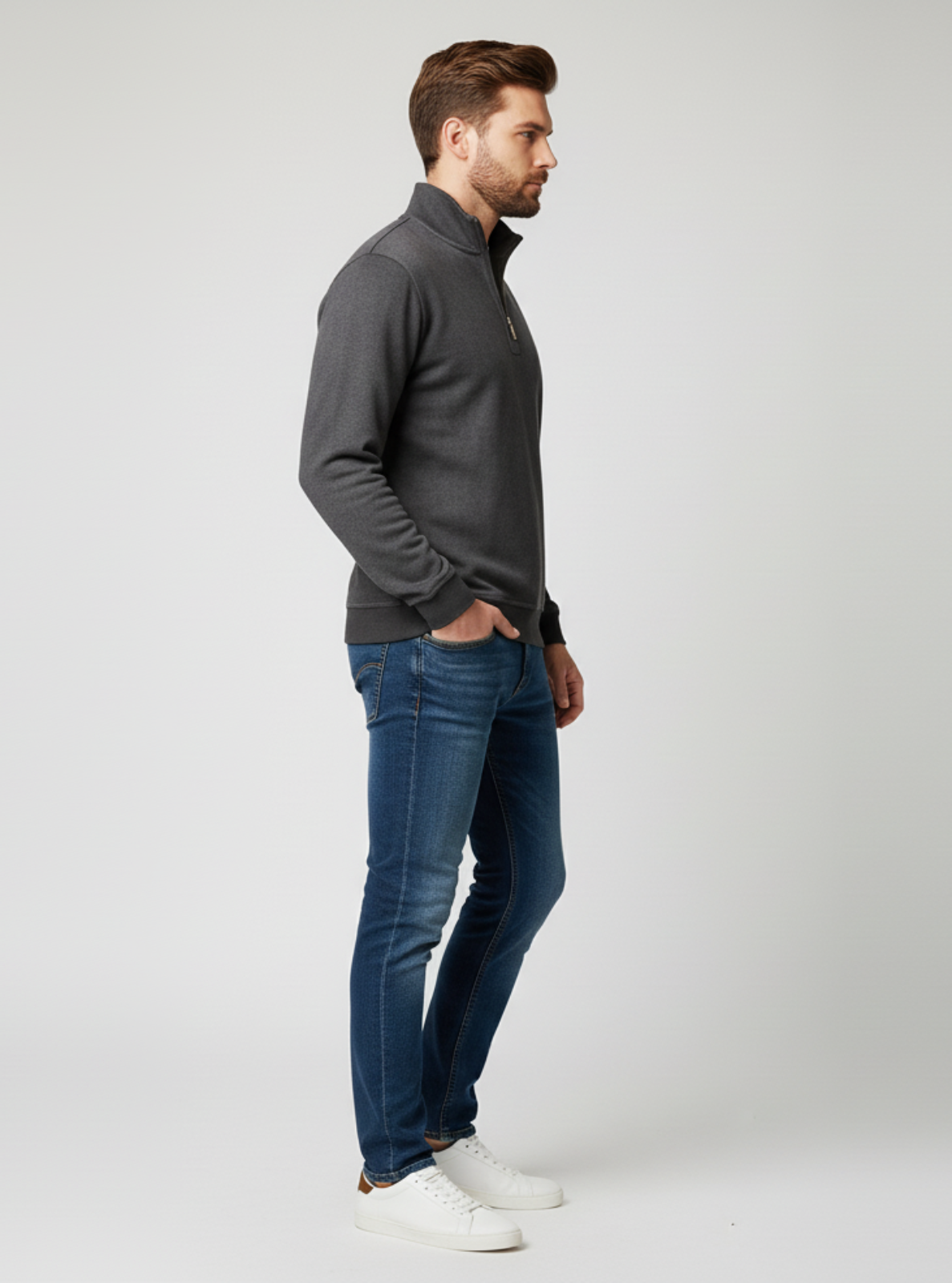 Man wearing a gray sweater, blue jeans, and white shoes on a light gray background